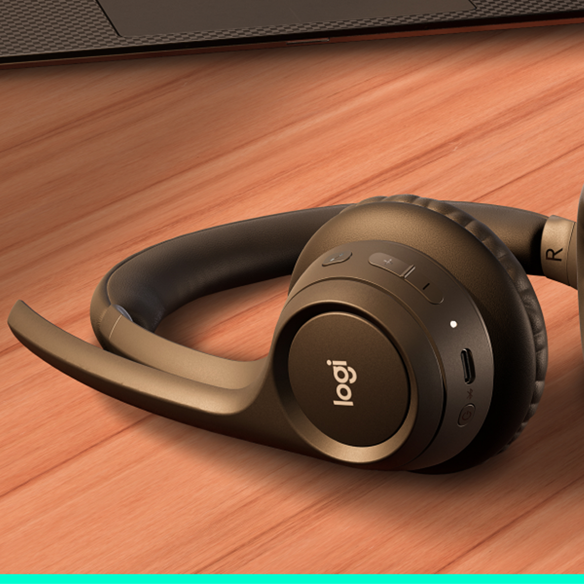 Brązowe słuchawki leżą na drewnianej powierzchni obok laptopa, prezentując swój wygląd i fakturę.