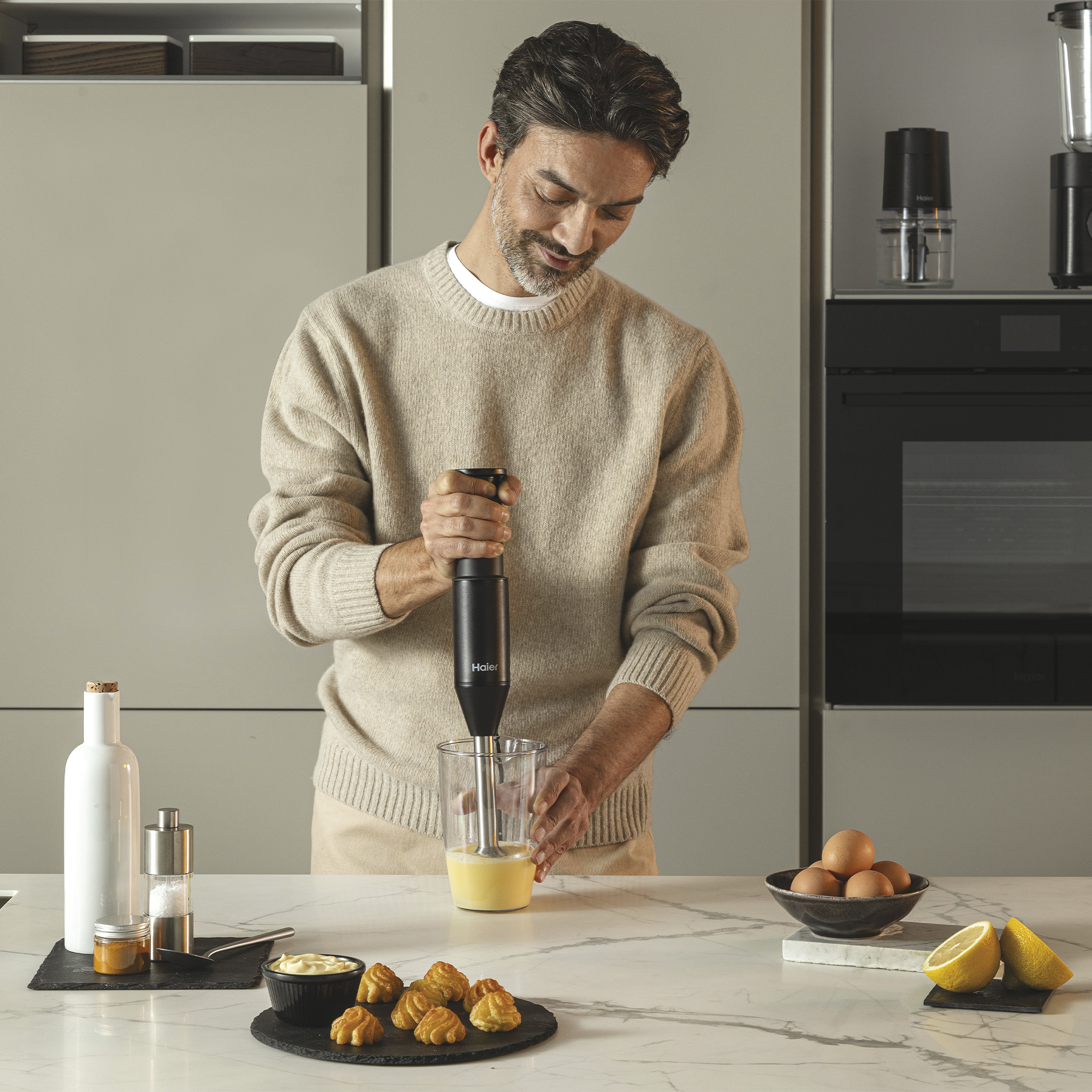 Mężczyzna miksuje składniki czarnym blenderem zanurzeniowym w nowoczesnej kuchni.