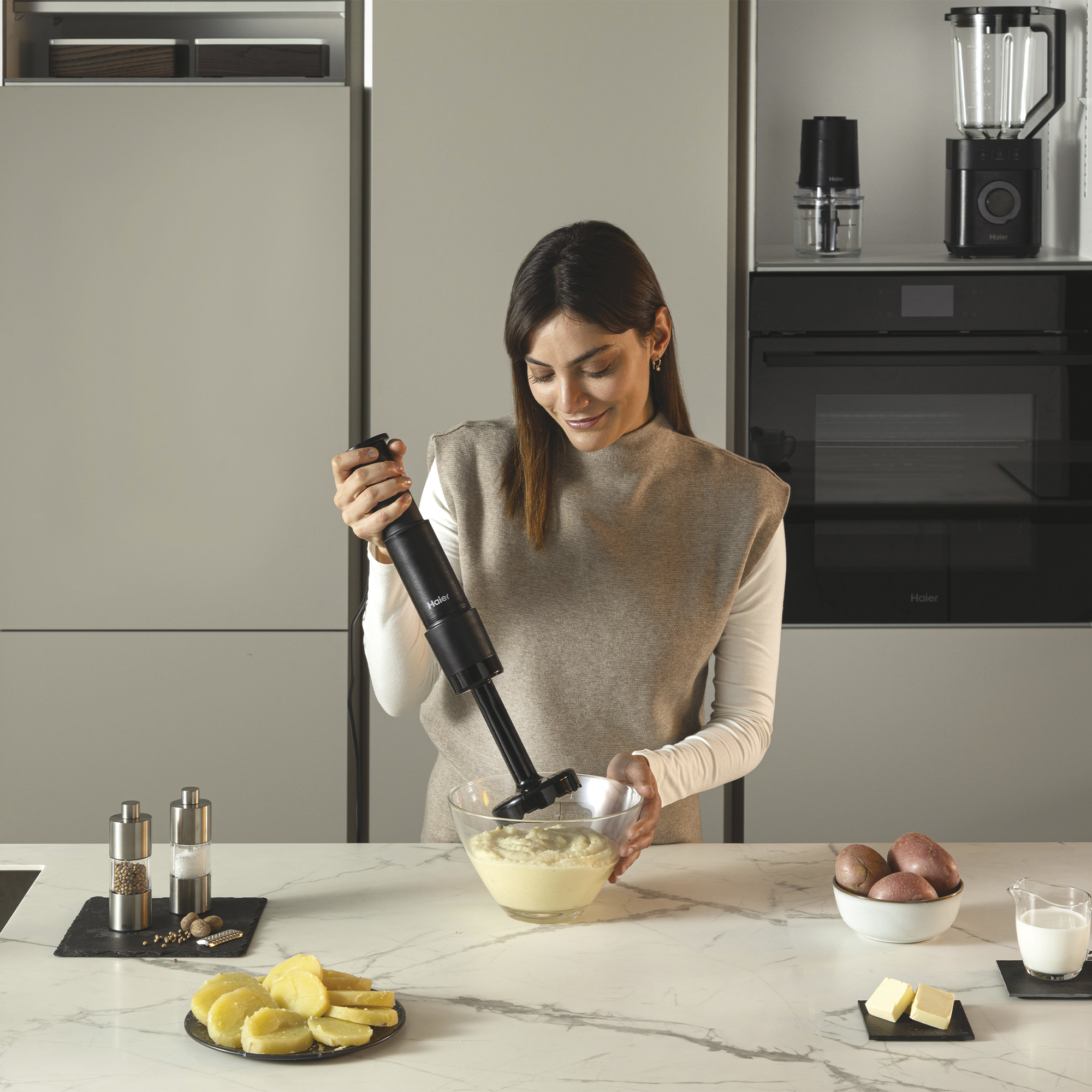 Kobieta miksuje ziemniaki czarnym blenderem zanurzeniowym w nowoczesnej kuchni.