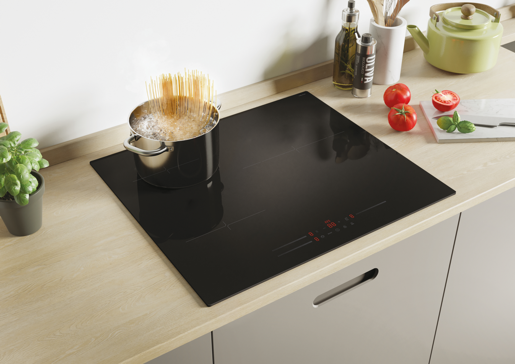 Spaghetti gotuje się na czarnej płycie indukcyjnej, z pobliskimi świeżymi składnikami.