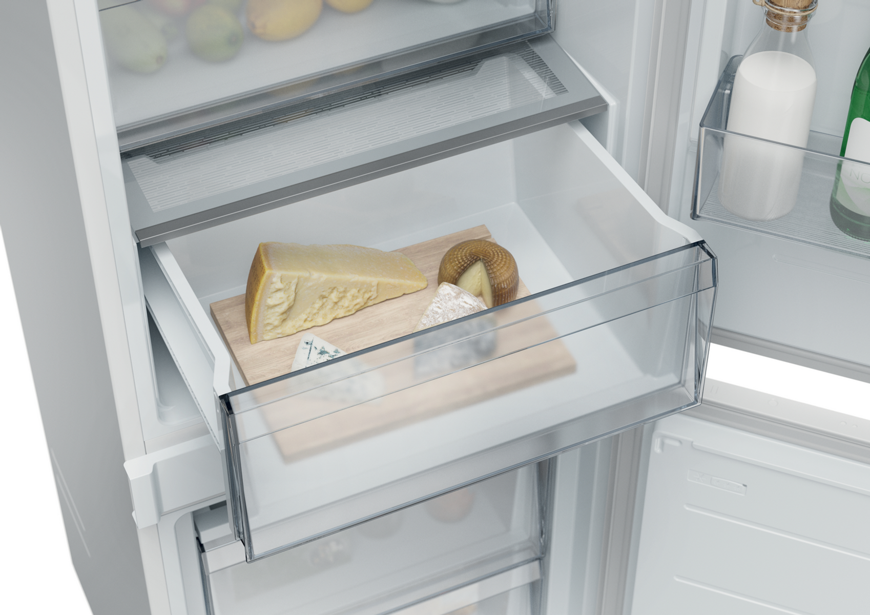 W szufladzie lodówki, kawałki sera i okrągły ser na drewnianej desce.