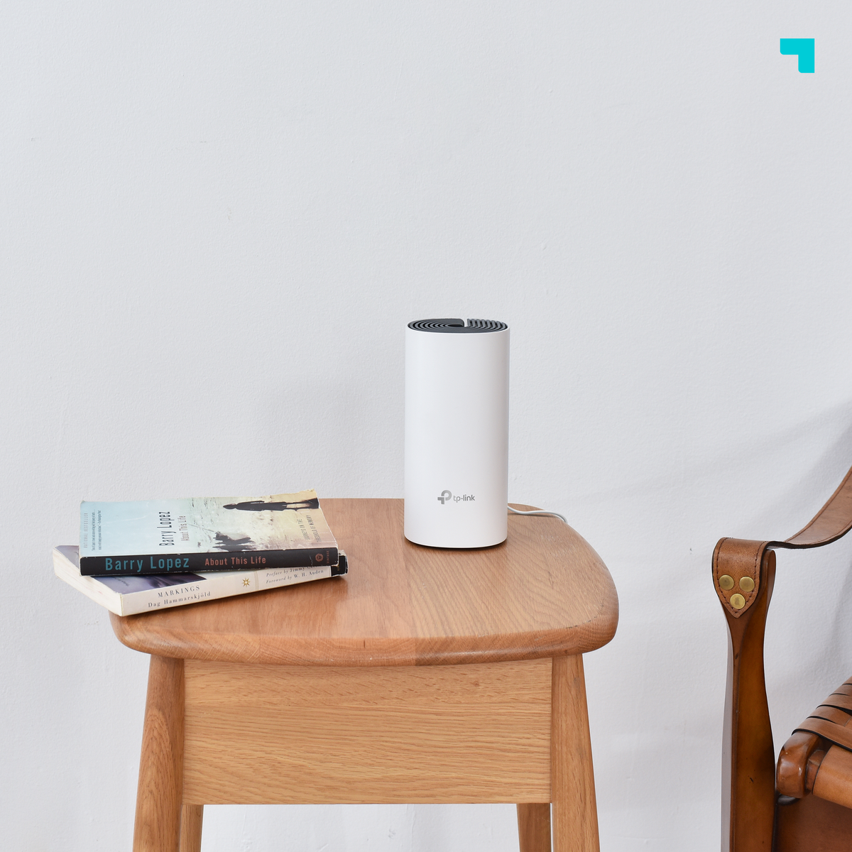 Een witte router staat op een houten tafel, naast twee boeken. Een bruine stoel rechts, witte muur op de achtergrond.