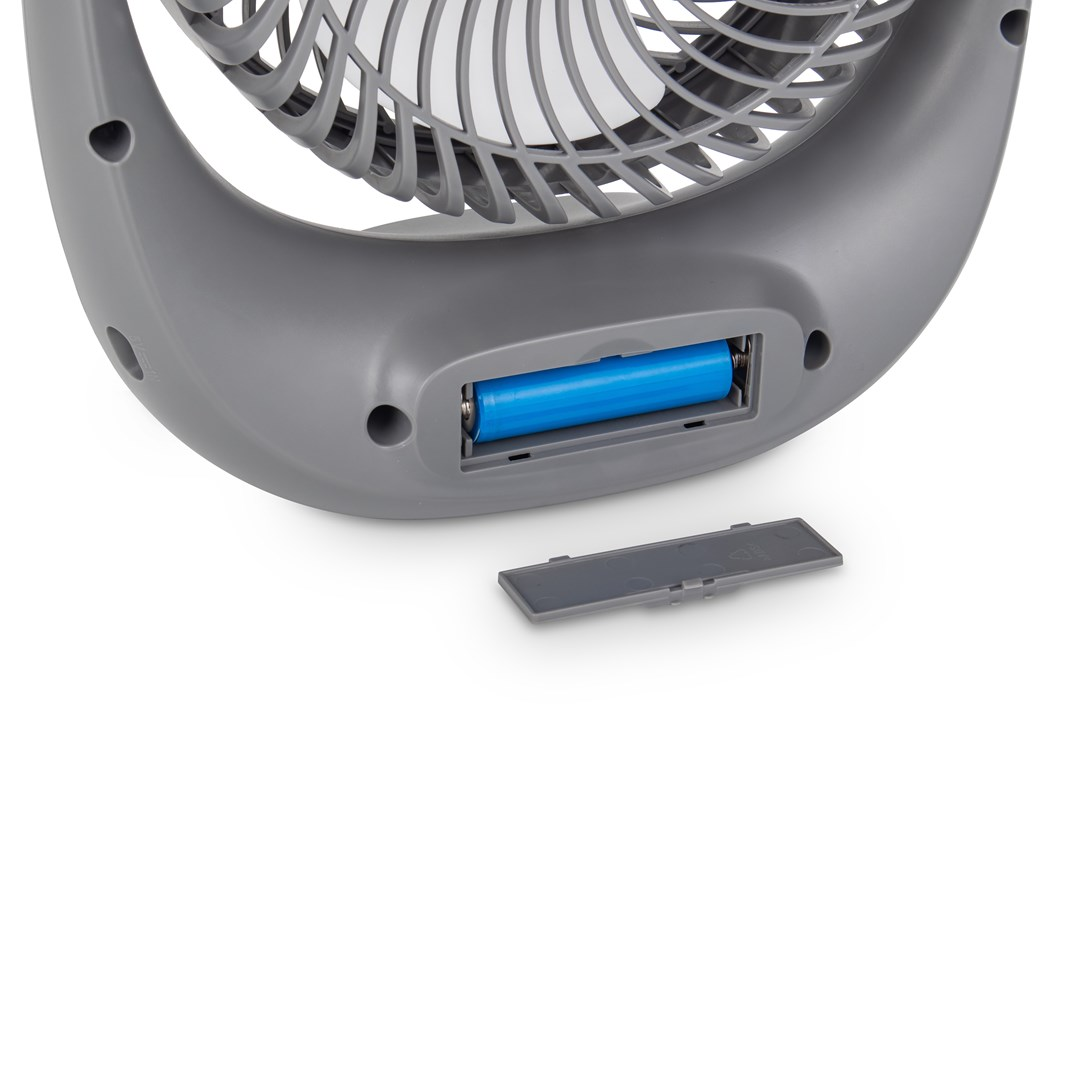 Un ventilateur gris avec un compartiment à piles bleu. Le ventilateur est sur une surface blanche.