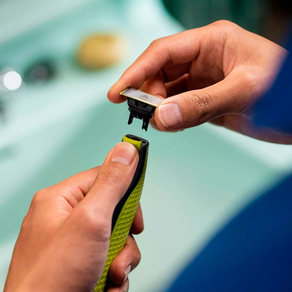 Ręce wyjmujące głowicę golarki z korpusu. Zielona i czarna golarka.