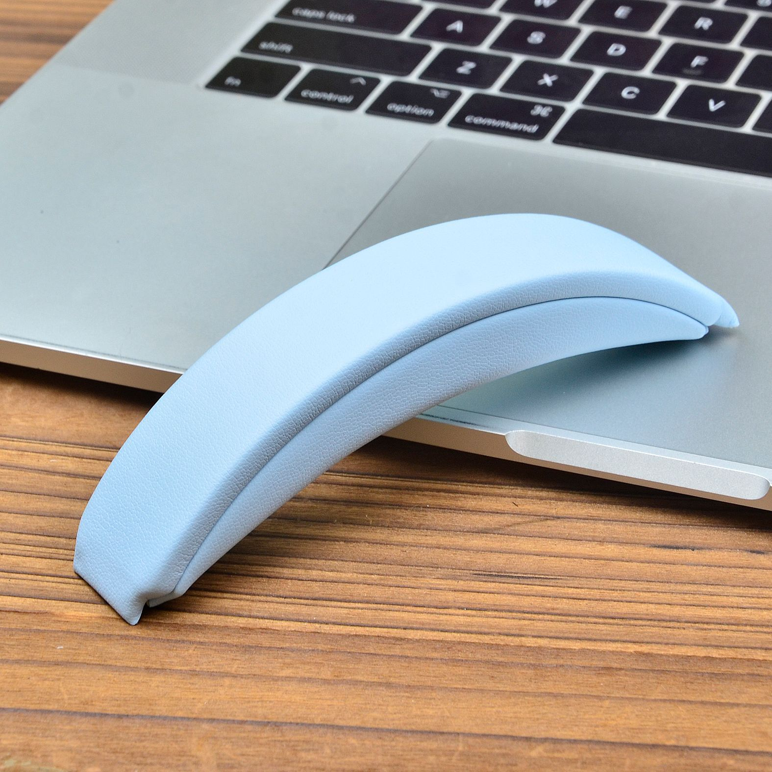 Un poggiapolsi azzurro chiaro è sopra un laptop argentato. Il laptop è su un tavolo di legno.