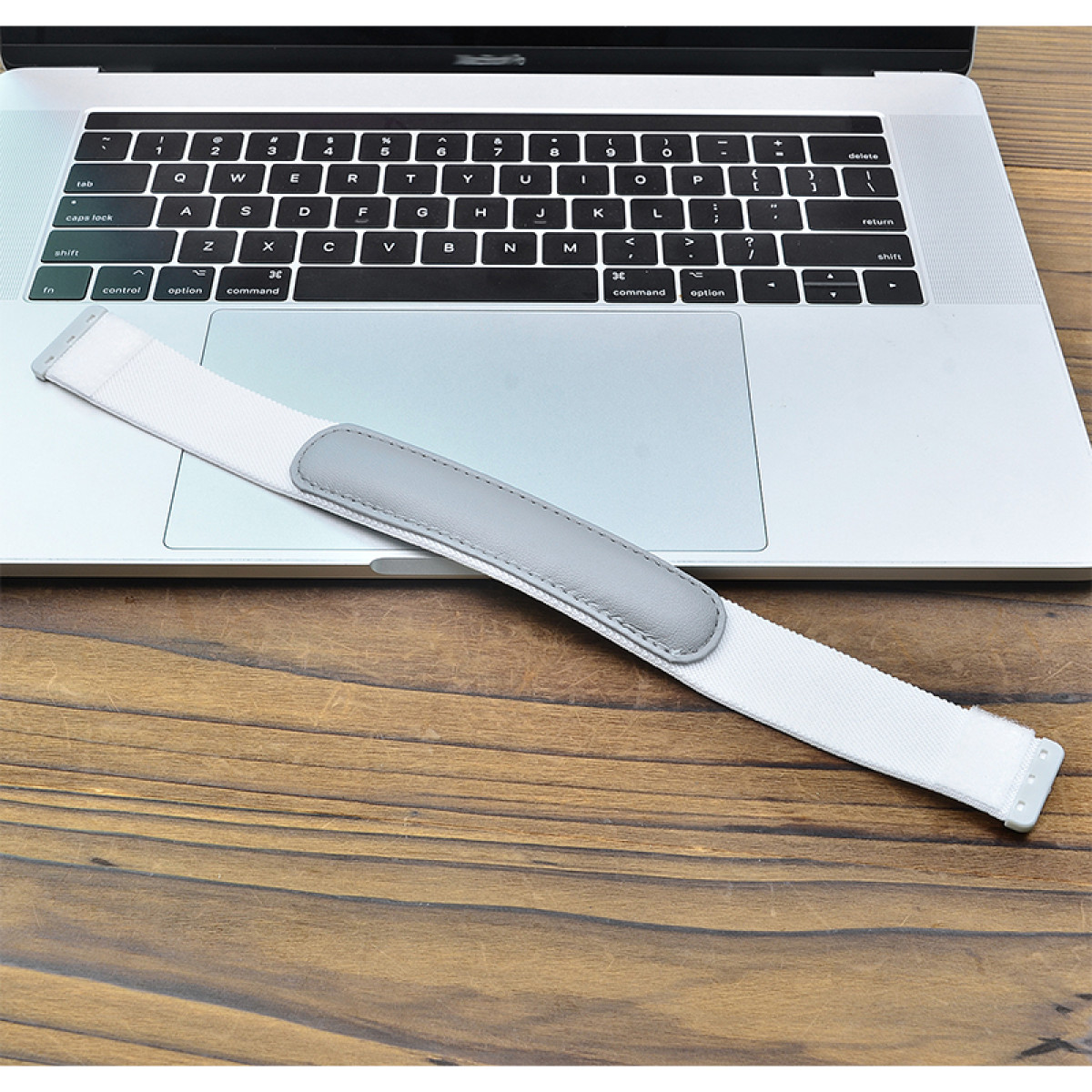 Ein weißes Kopfband mit grauem Polster liegt auf einer Laptop-Tastatur auf Holz.