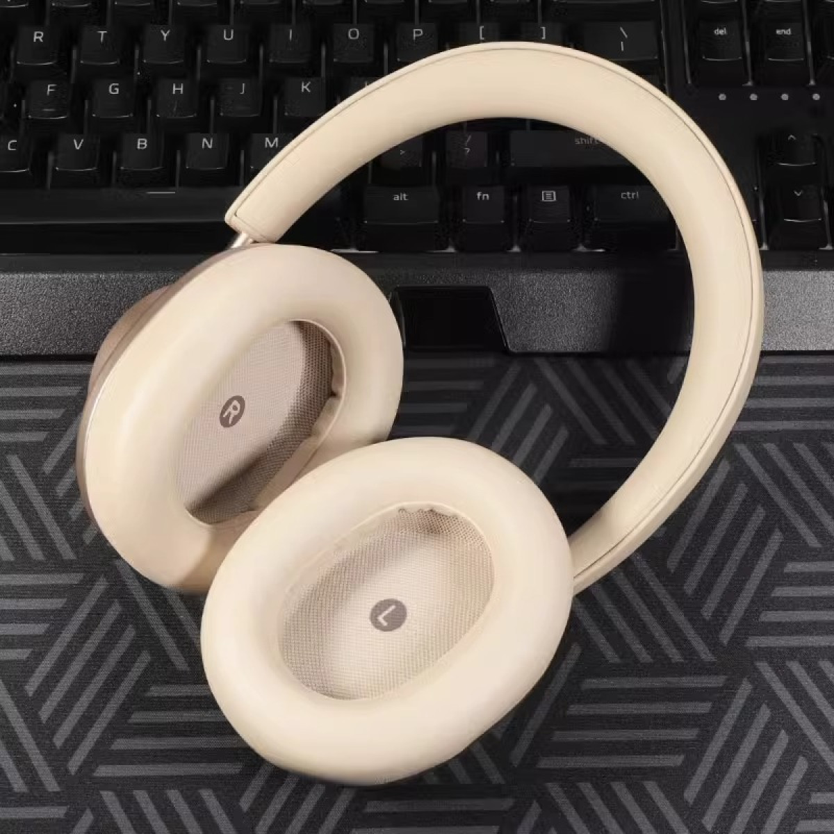Cuffie con padiglioni e archetto beige, su una superficie scura, vicino a una tastiera. Sul padiglione destro una 'R'.