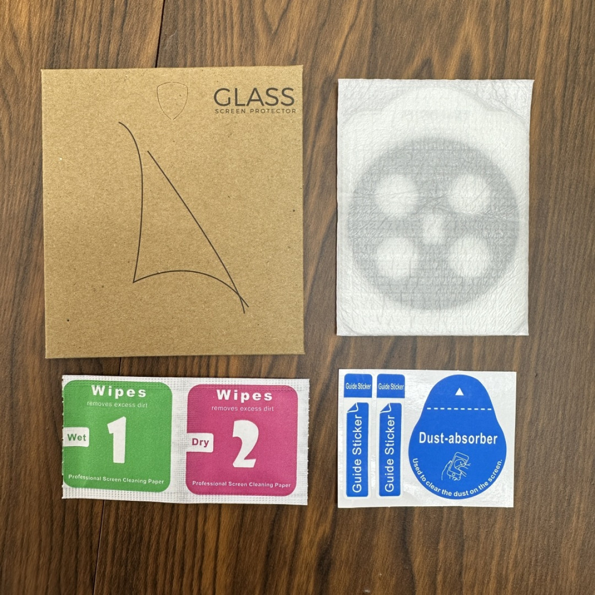 Un set di accessori per la protezione dello schermo su una superficie in legno. Include salviette, adesivi guida e pulizia.