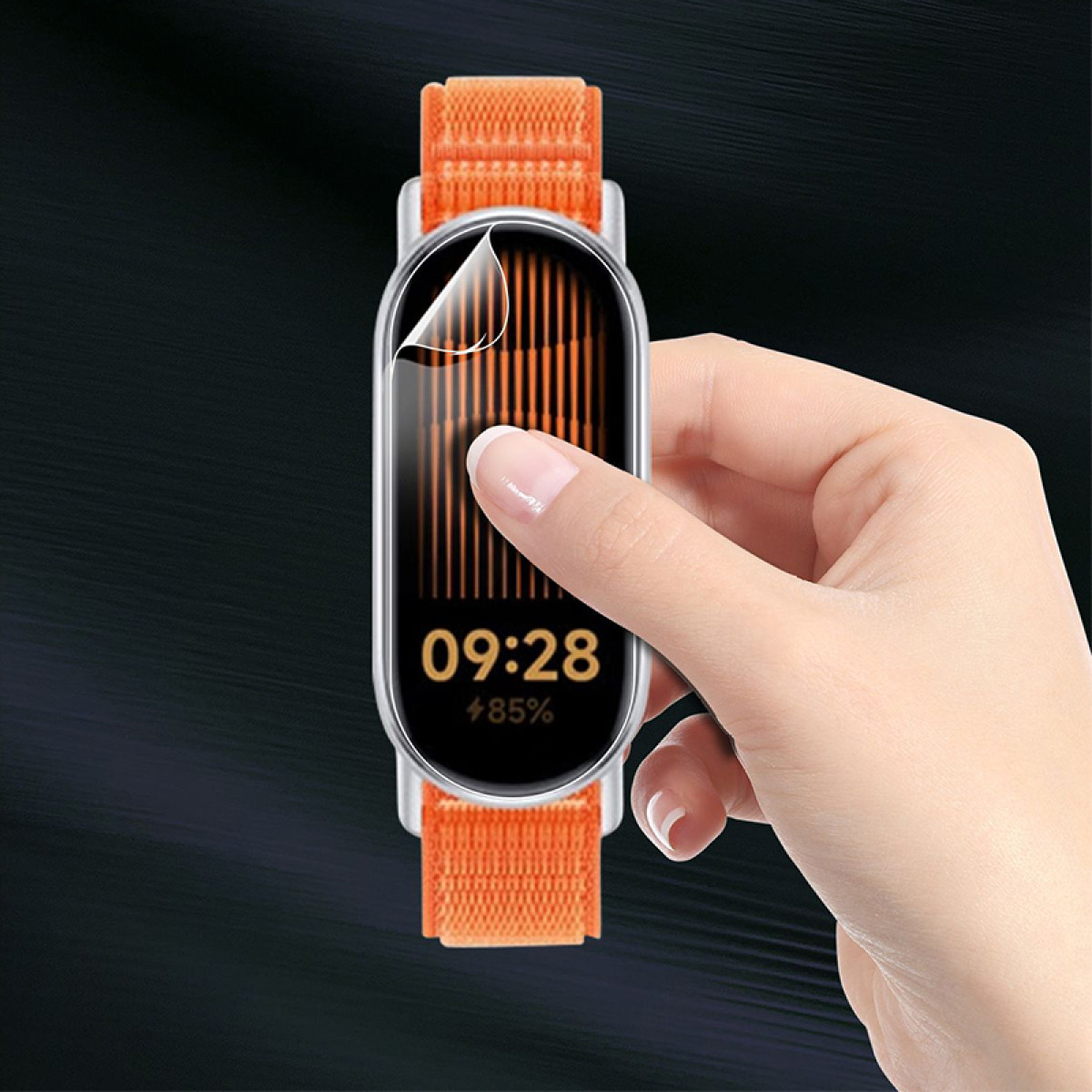 Una mano applica una protezione schermo a uno smartwatch con cinturino arancione. Lo schermo mostra dati e orologio digitale.