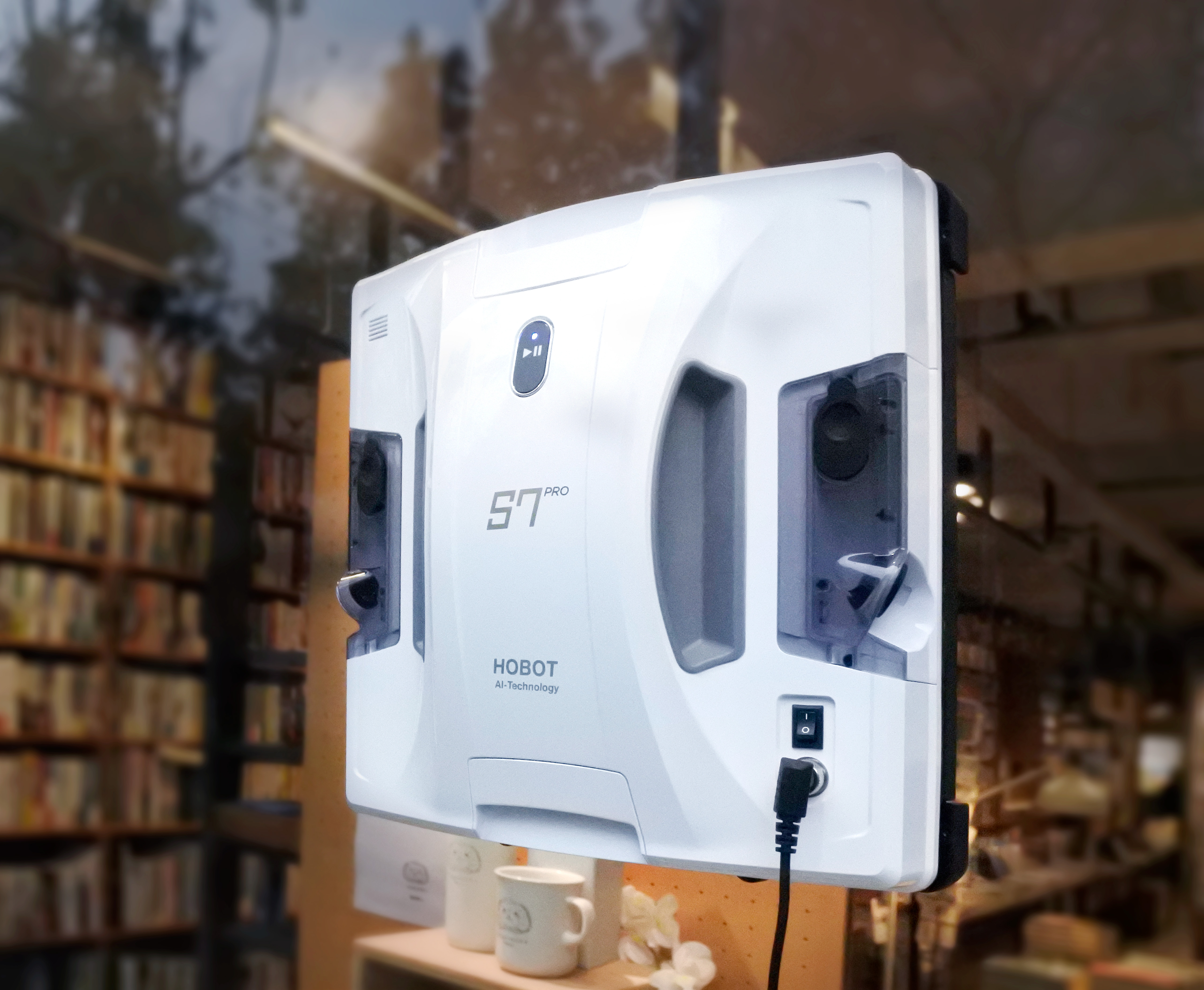 Un robot limpiacristales blanco en una librería con una taza.