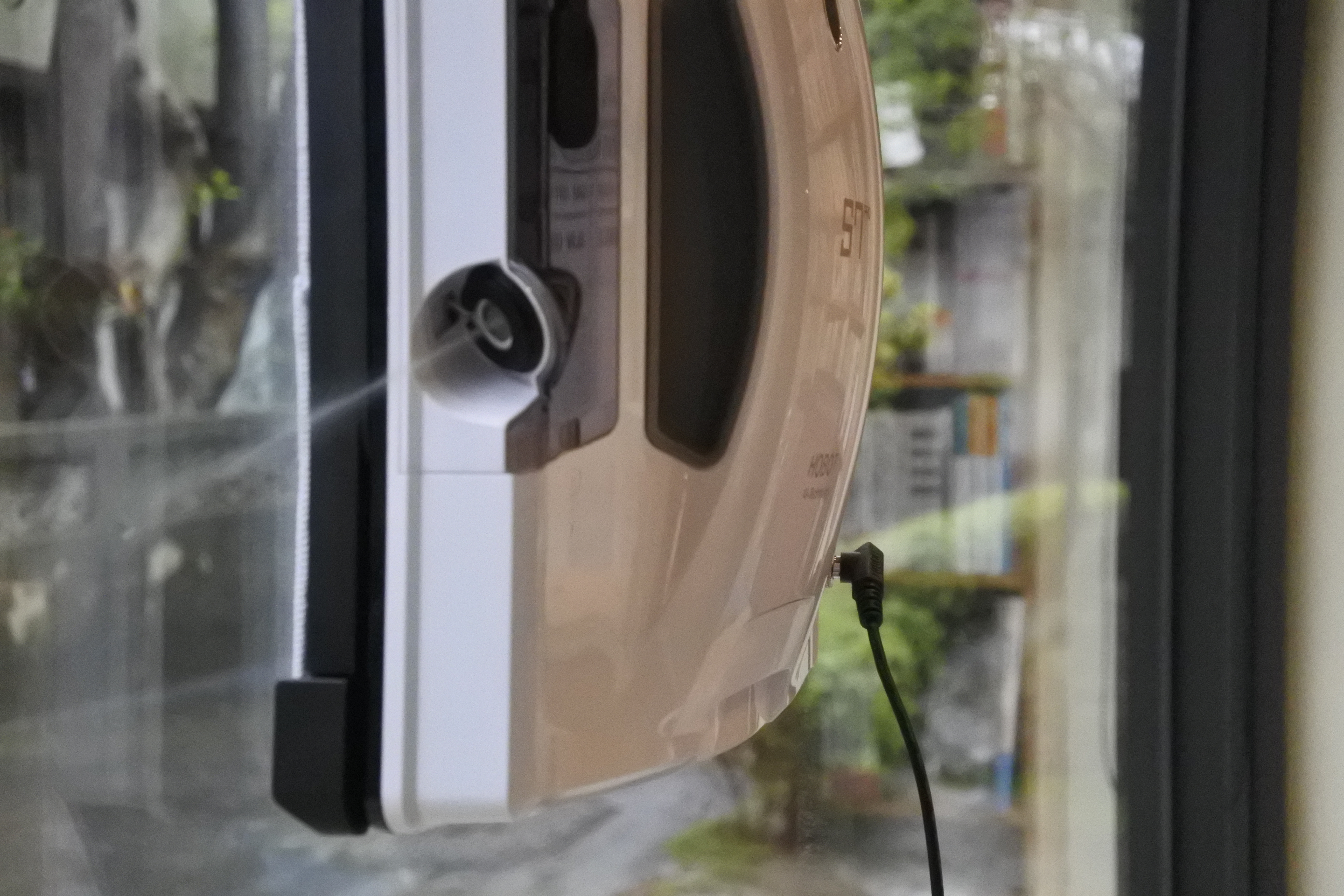 Un robot limpiacristales está adherido a una ventana, conectado por cable.