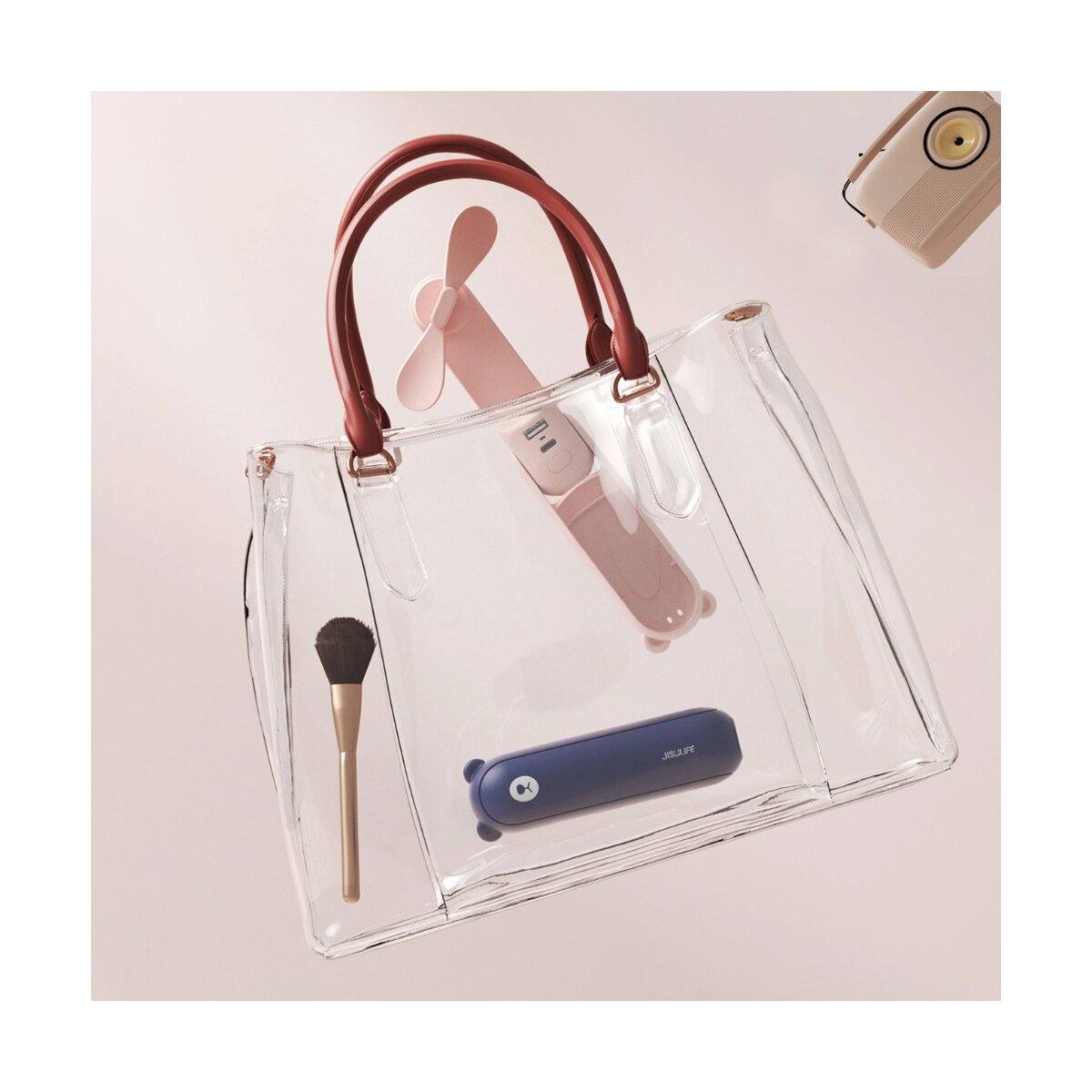 Transparente Handtasche mit einem kleinen rosa Ventilator, einem blauen Ventilator, einem Pinsel und einem Radio. Alles in der Tasche.