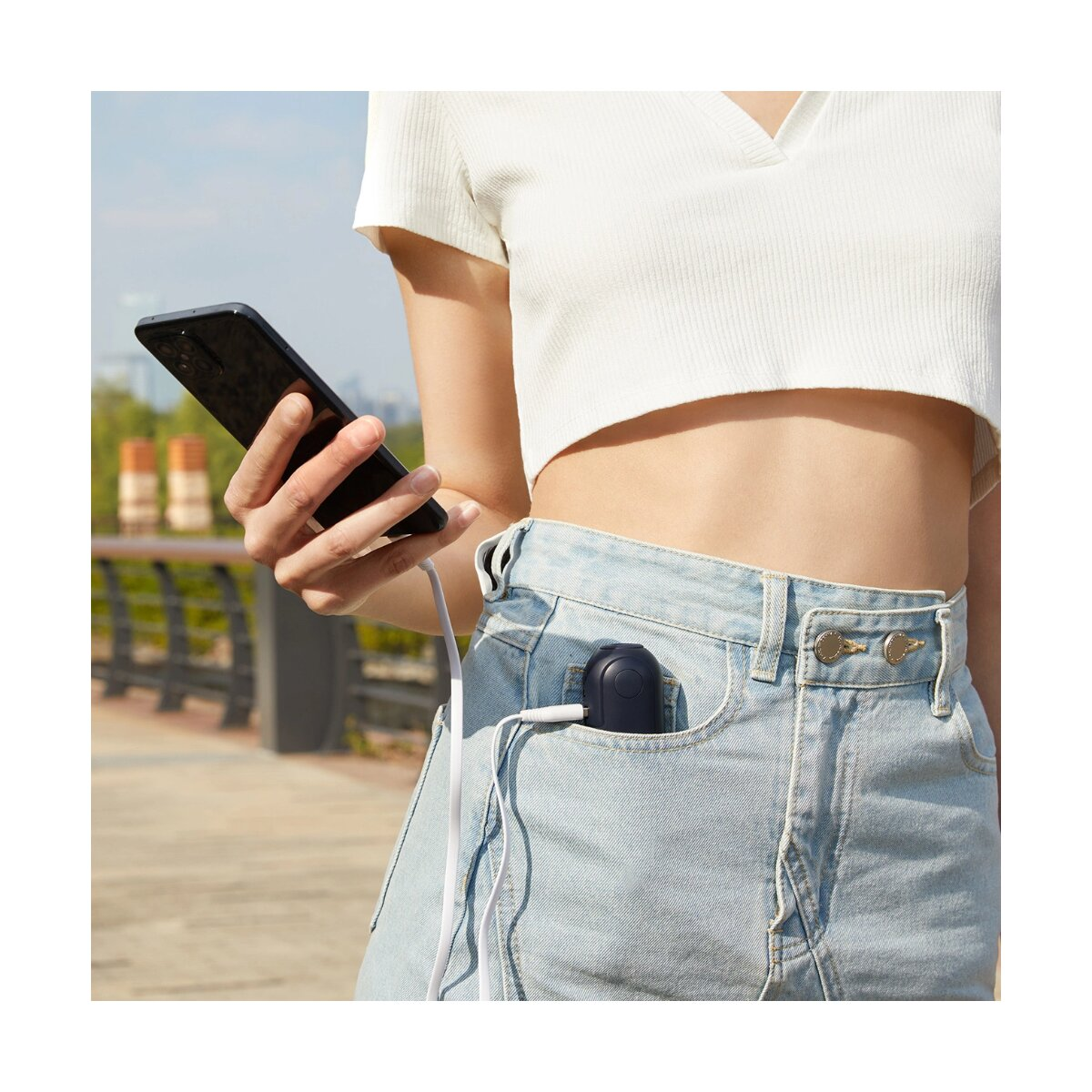 Eine Person, die ein schwarzes Telefon hält, mit einem tragbaren Ventilator in der Tasche, der mit einem Kabel verbunden ist.