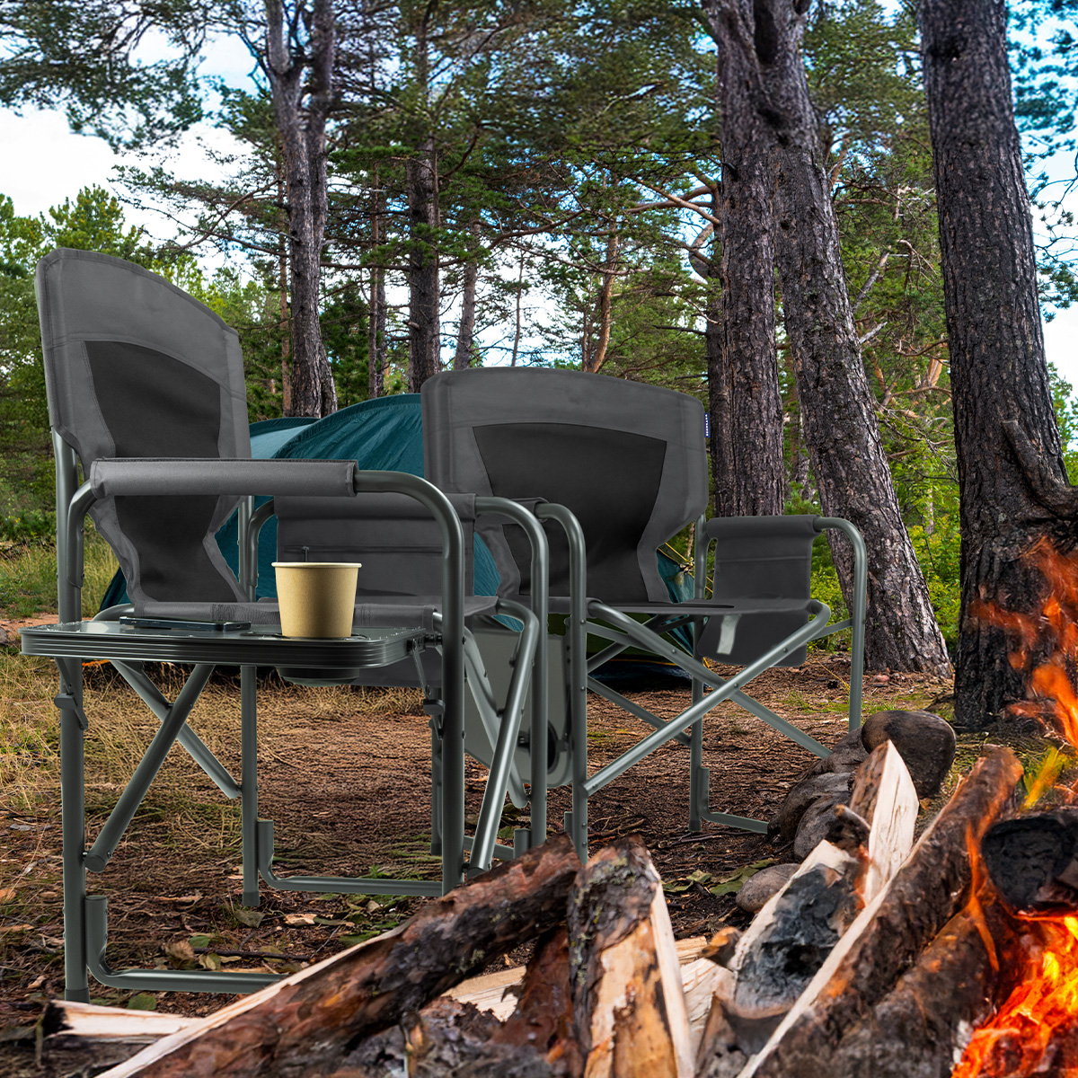 Camping chairs and table set in a forest. Fire and trees are in the background.