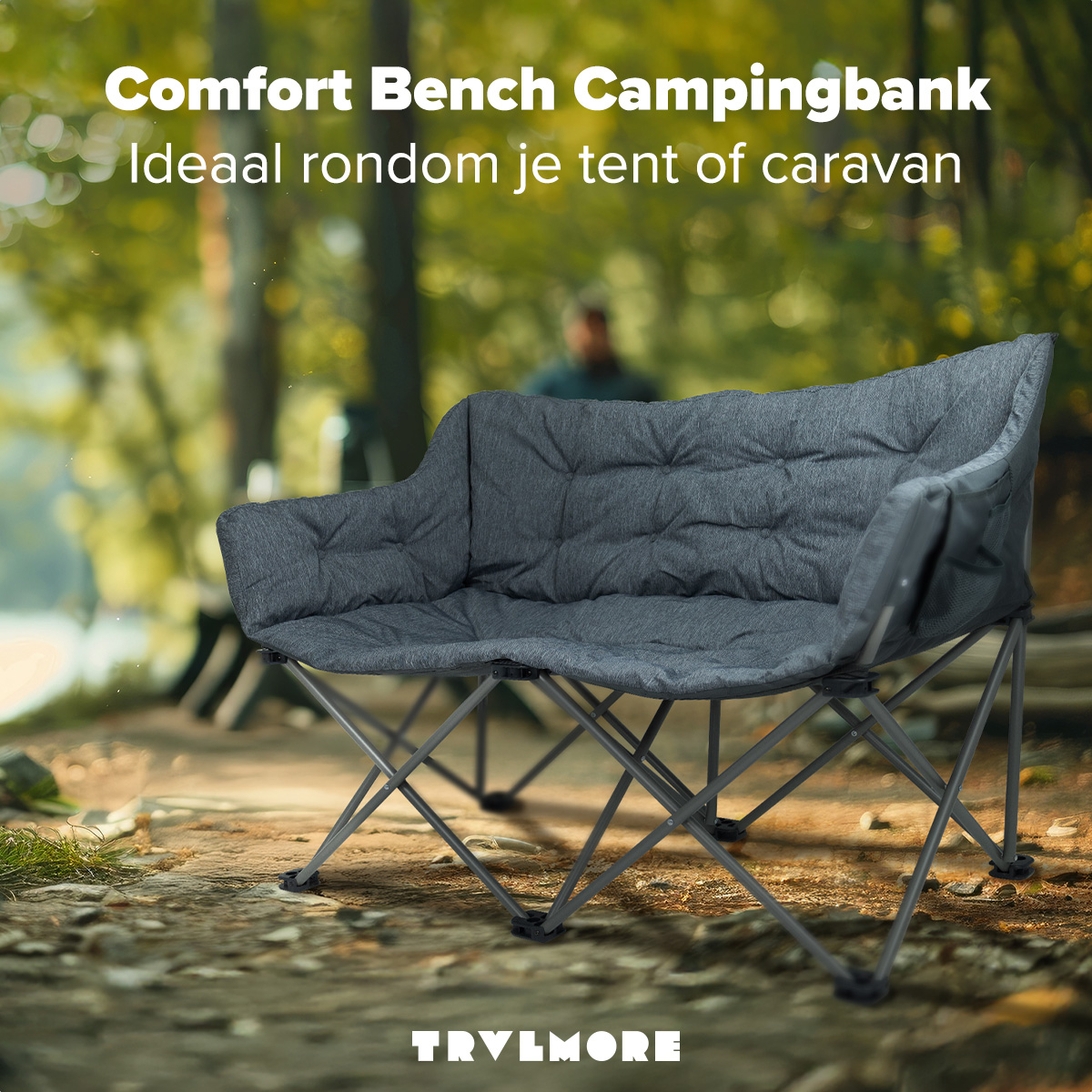 Gray camping bench on a grassy area near trees. Text above reads 'Comfort Bench Campingbank'. Text at the bottom: 'TRVLMORE'.