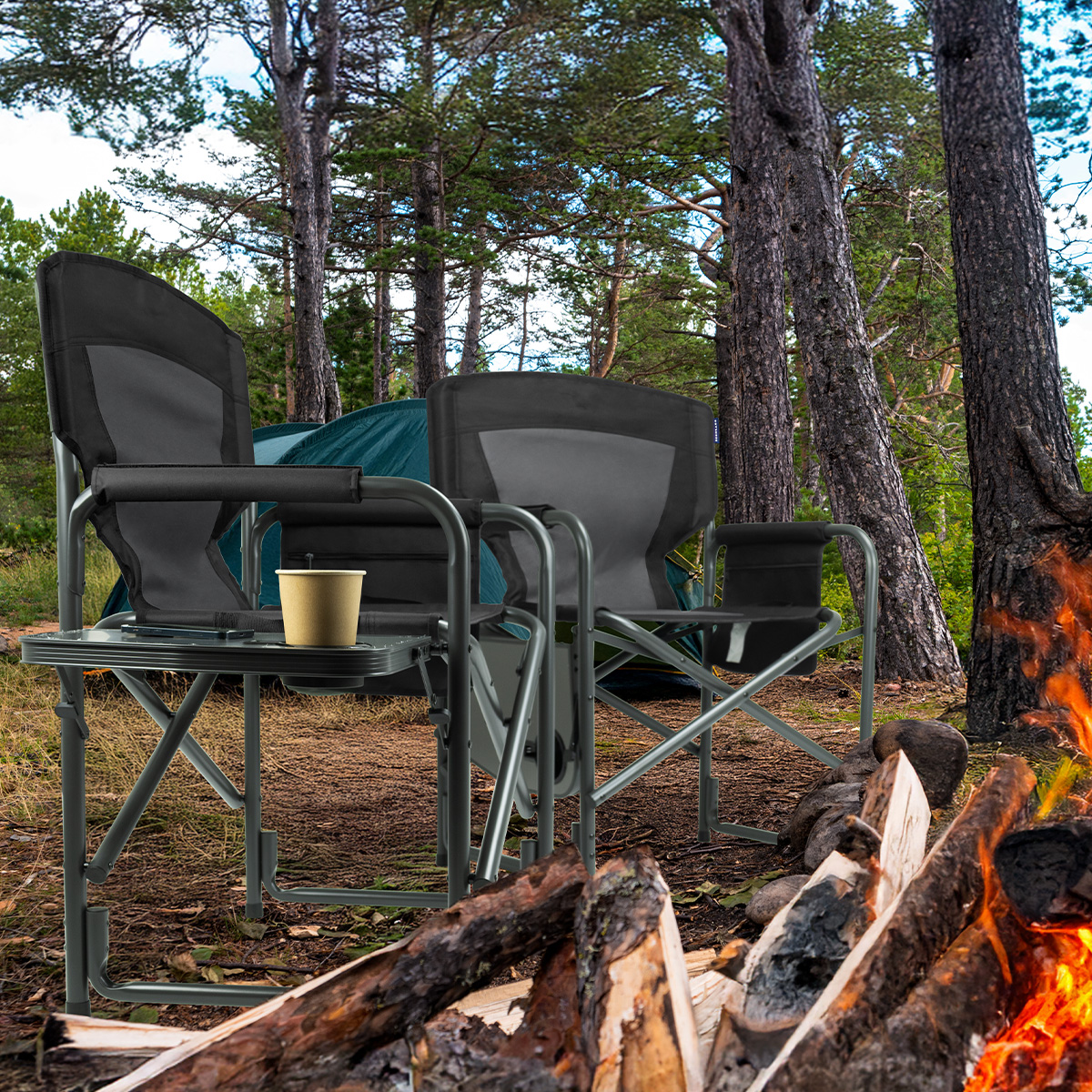 Camping scene with two chairs, a table, and a campfire. Trees in the background with a green tent. Burning fire.