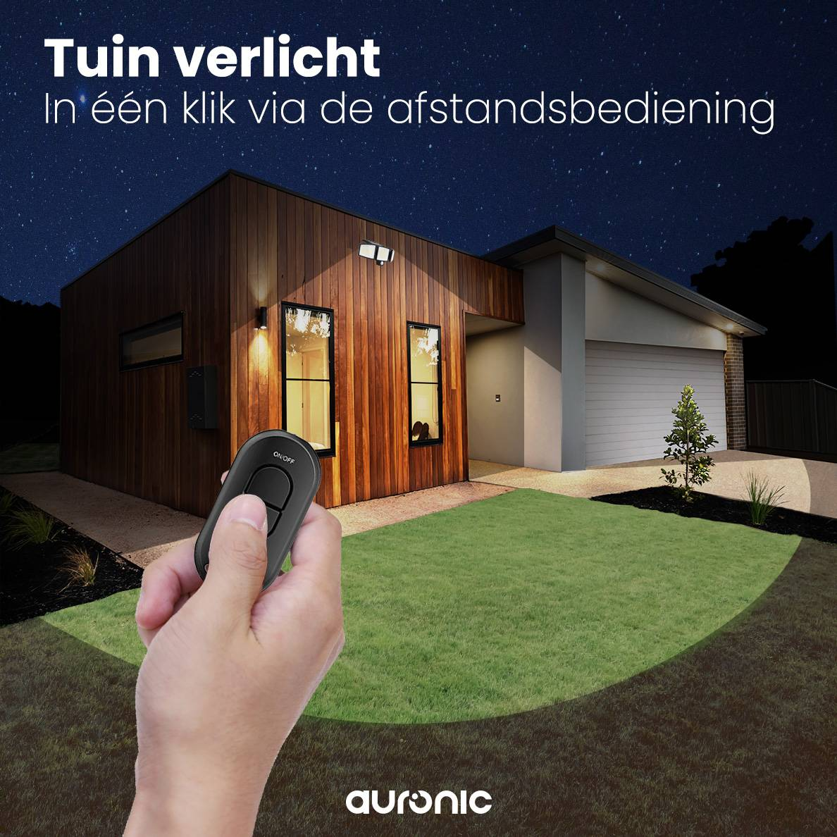 A hand holding a remote control pointing towards a house at night. The lawn is illuminated with a green light.