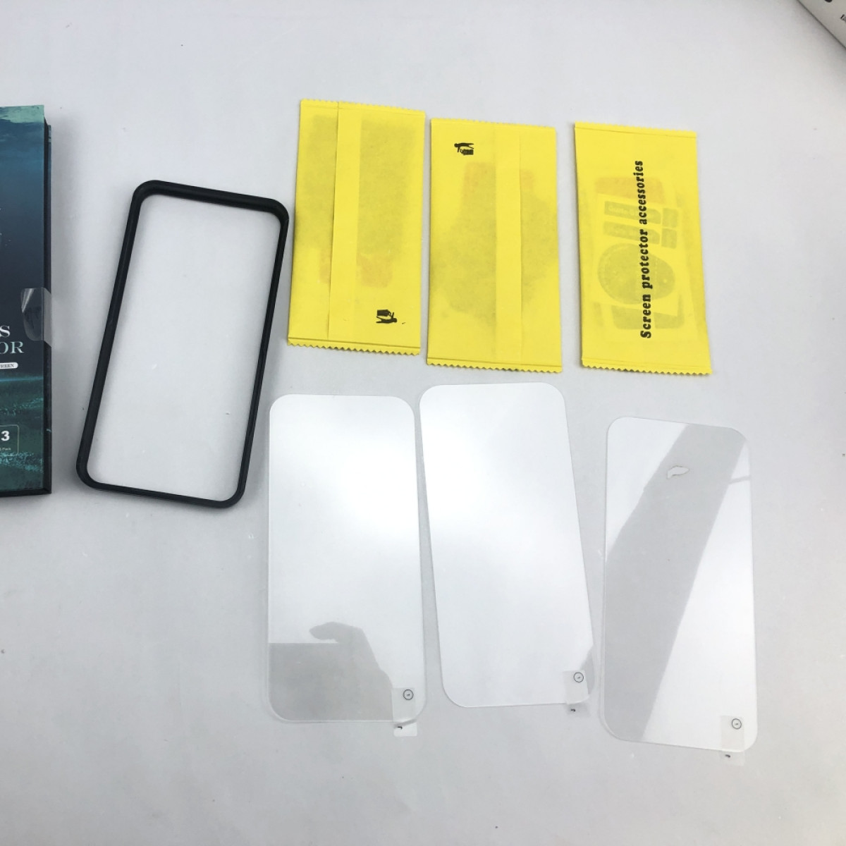Vari accessori per protezioni schermo sono organizzati su una superficie bianca. L'attenzione è sui prodotti.