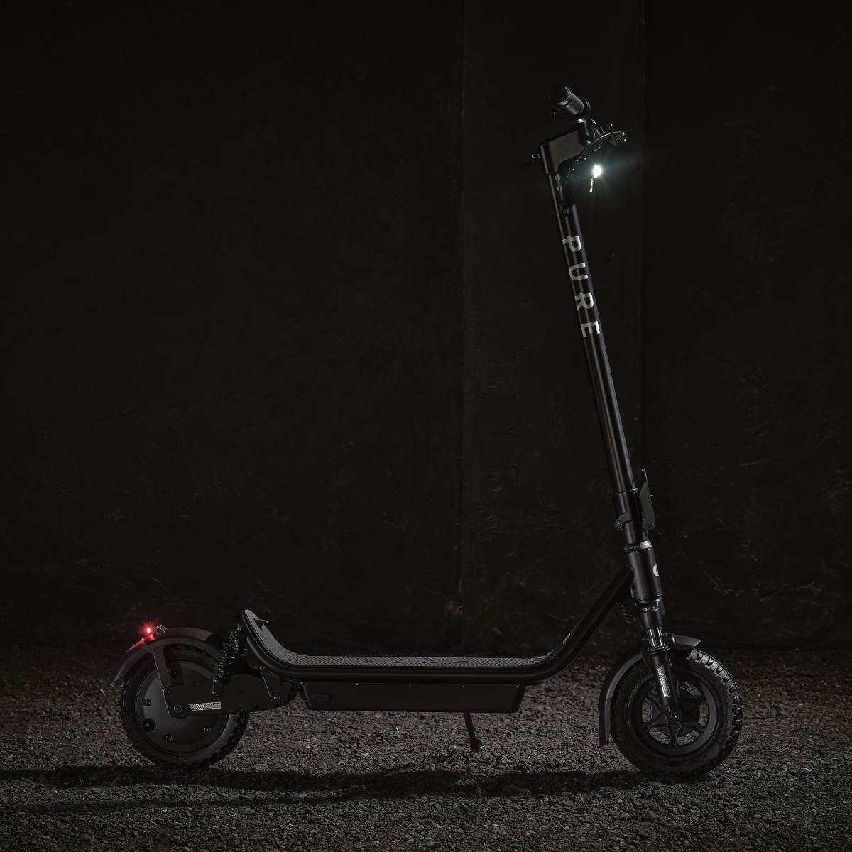 Schwarzer Roller, beleuchtet von Scheinwerfer und Rücklicht. Auf strukturierter Oberfläche, vor dunklem Hintergrund.