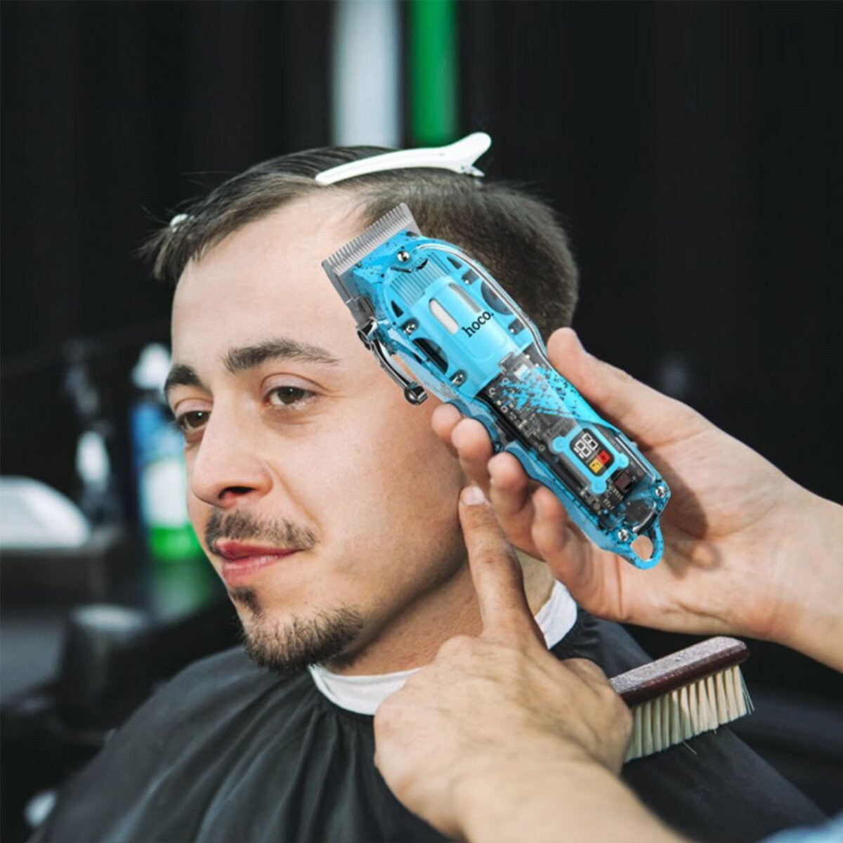 Ein Friseur, der einem Mann einen blauen Haarschneider benutzt. Eine Bürste liegt auf dem Hals des Mannes.