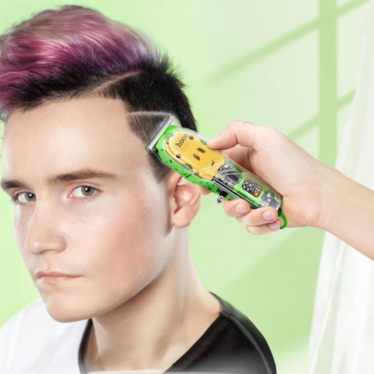 Eine Hand benutzt einen grünen Haarschneider an den Haaren einer Person. Der Rasierer ist gelb und grün.