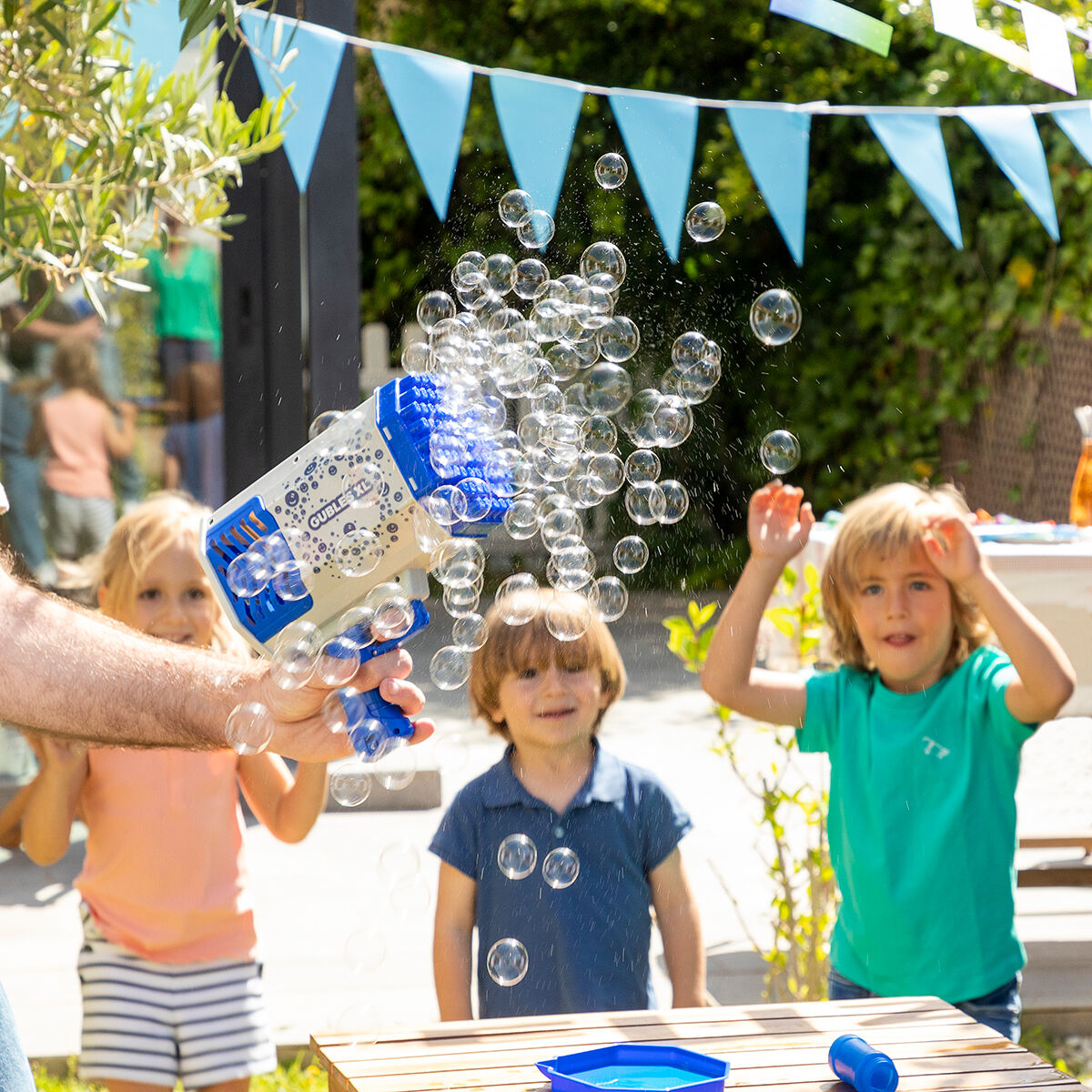 Kinder spielen mit einer Seifenblasenpistole. Seifenblasen fliegen in der Luft. Blaue Banner im Hintergrund.