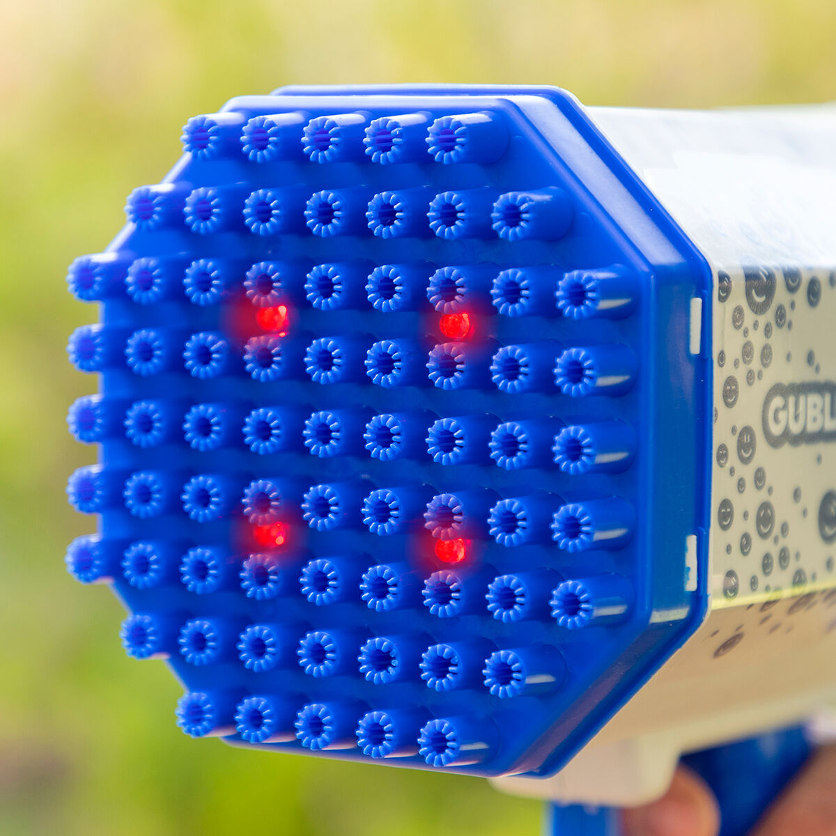 Blaue Blasenpistole mit vielen kleinen Löchern, Licht im Inneren und grünem Hintergrund.