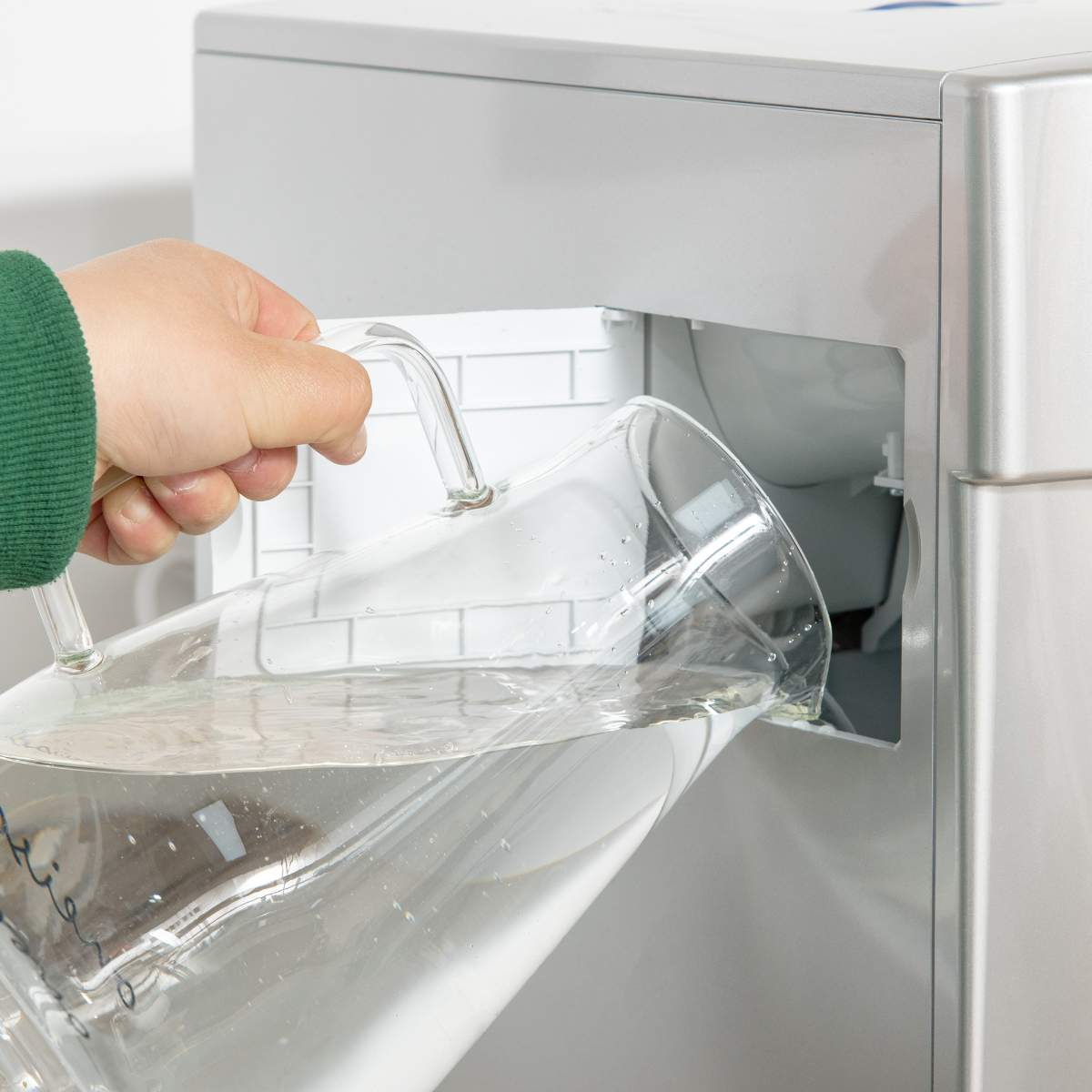 Person gießt Wasser aus einem Glaskrug in die Eismaschine.