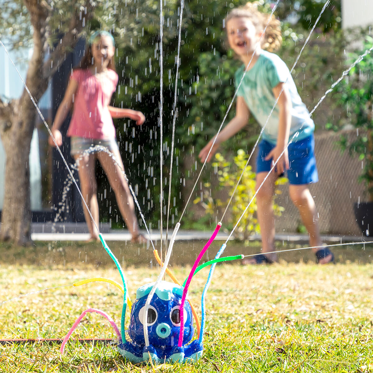 Ein blaues Oktopus-Spielzeug verspritzt Wasser auf einen Rasen, mit zwei Kindern im Hintergrund.