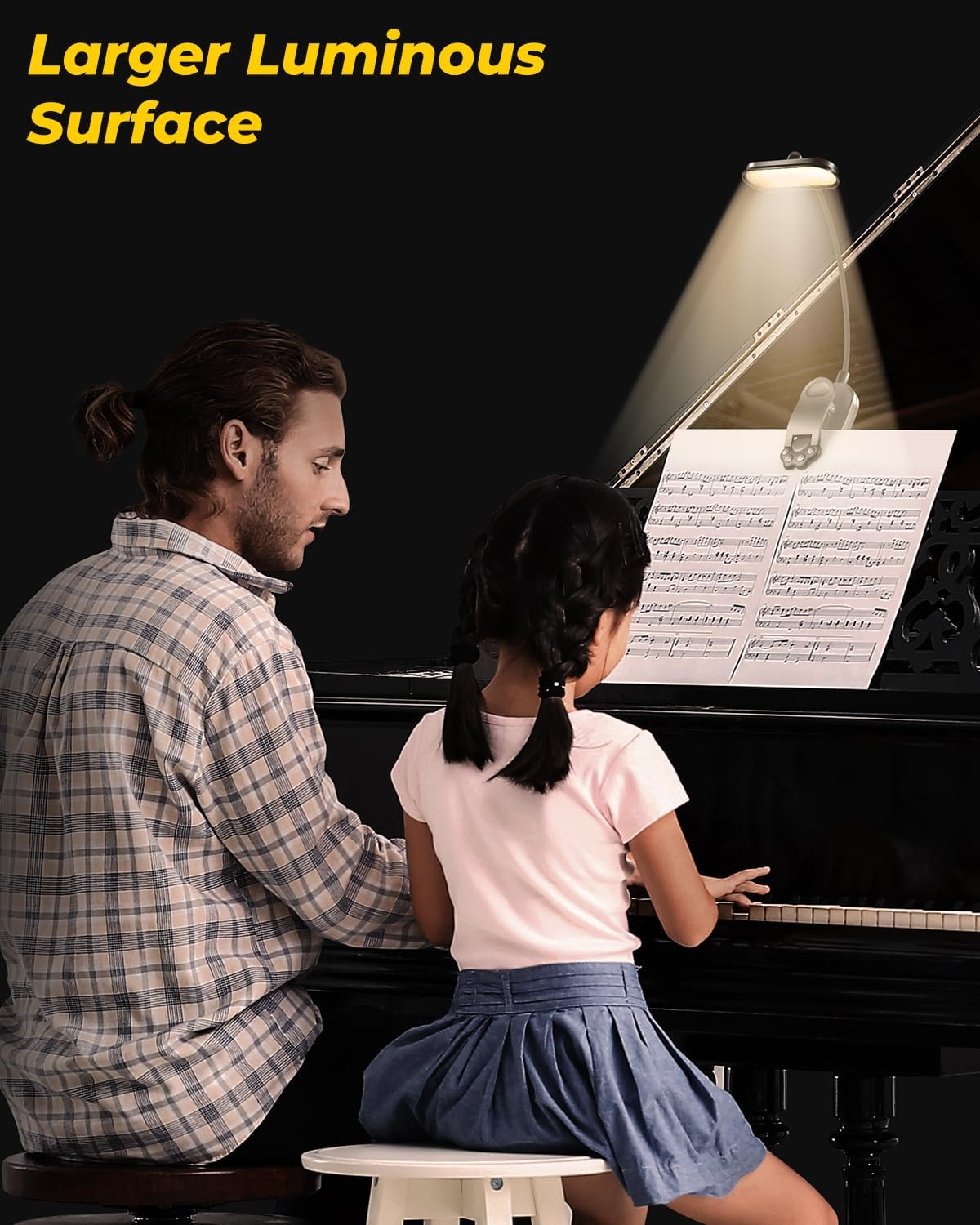 Ein Vater und eine Tochter am Klavier, mit einer Buchlampe, die Noten beleuchtet.