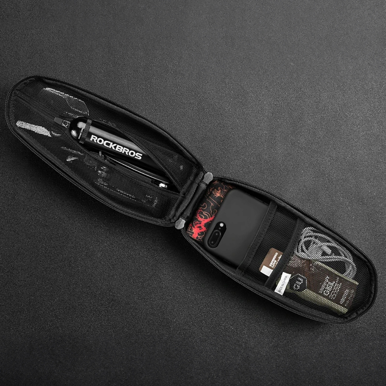 Otwarta torba na skuter z przedmiotami w środku: telefonem, kartami, kablami na czarnym tle.