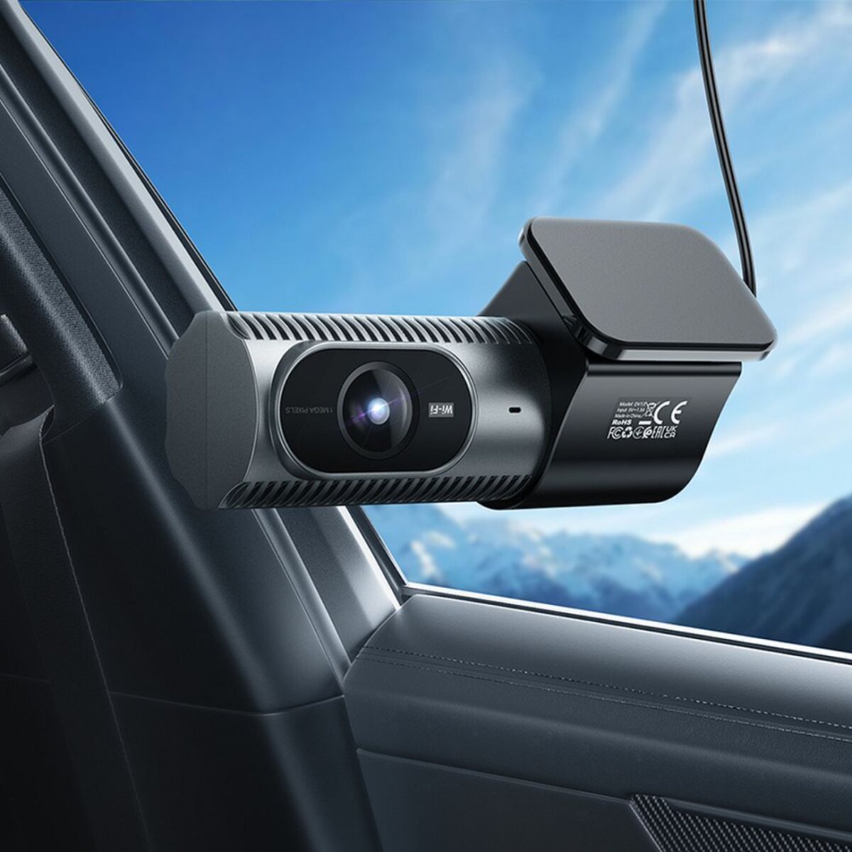 Eine Dashcam ist an einem Autofenster mit einem malerischen Hintergrund aus Bergen und blauem Himmel befestigt.