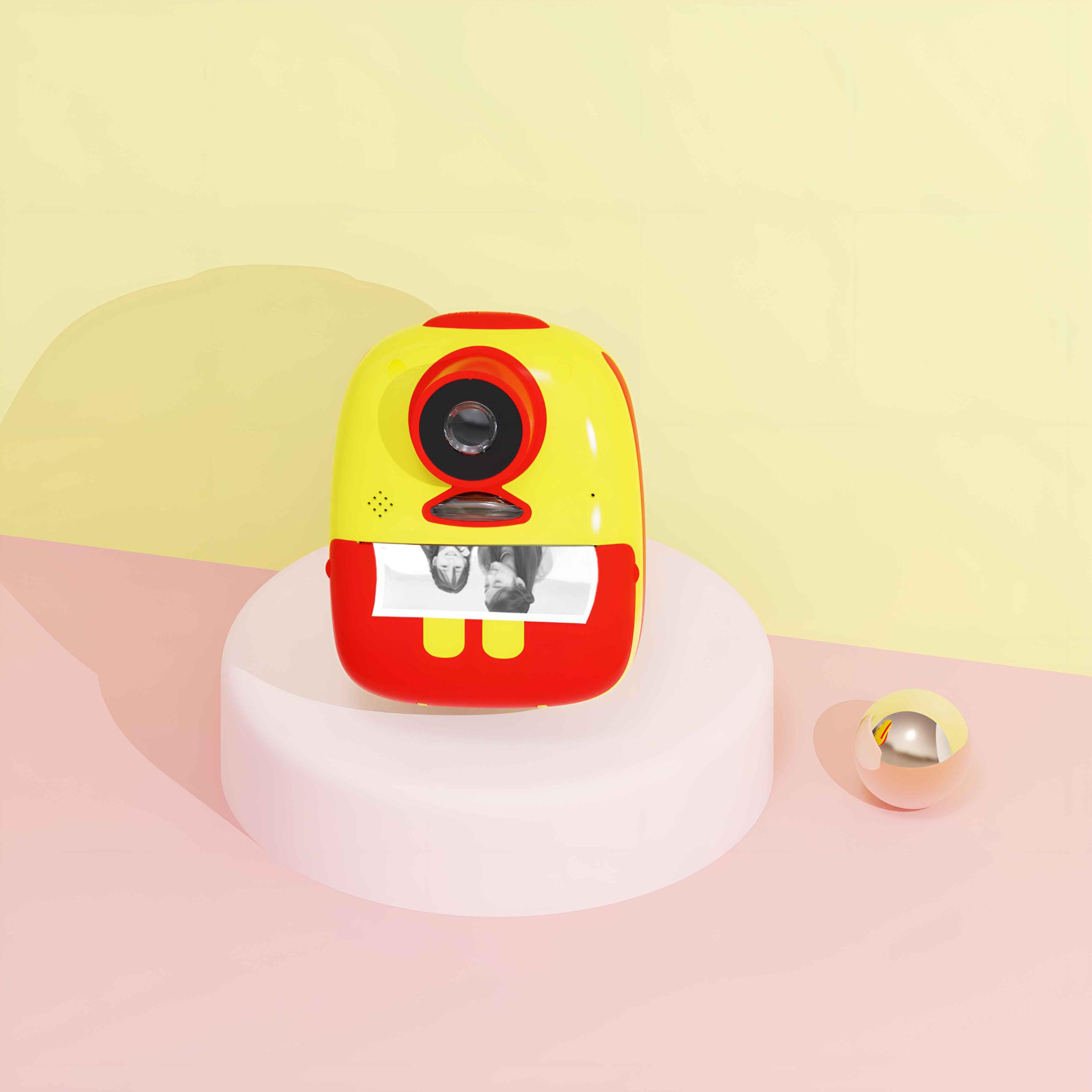 Eine gelb-rote Spielzeugkamera auf einer weißen Plattform, druckt ein Foto eines Paares, goldener Ball daneben.