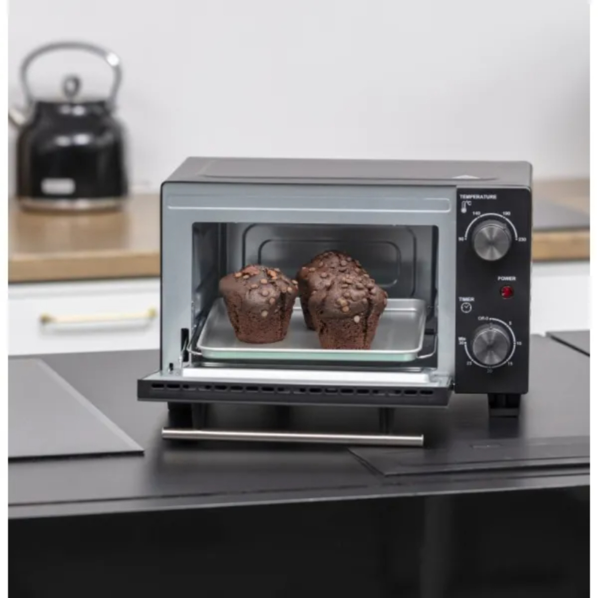 MPM Mini-Backofen mit offener Tür, enthält zwei Muffins auf einem Backblech, auf einer schwarzen Oberfläche.