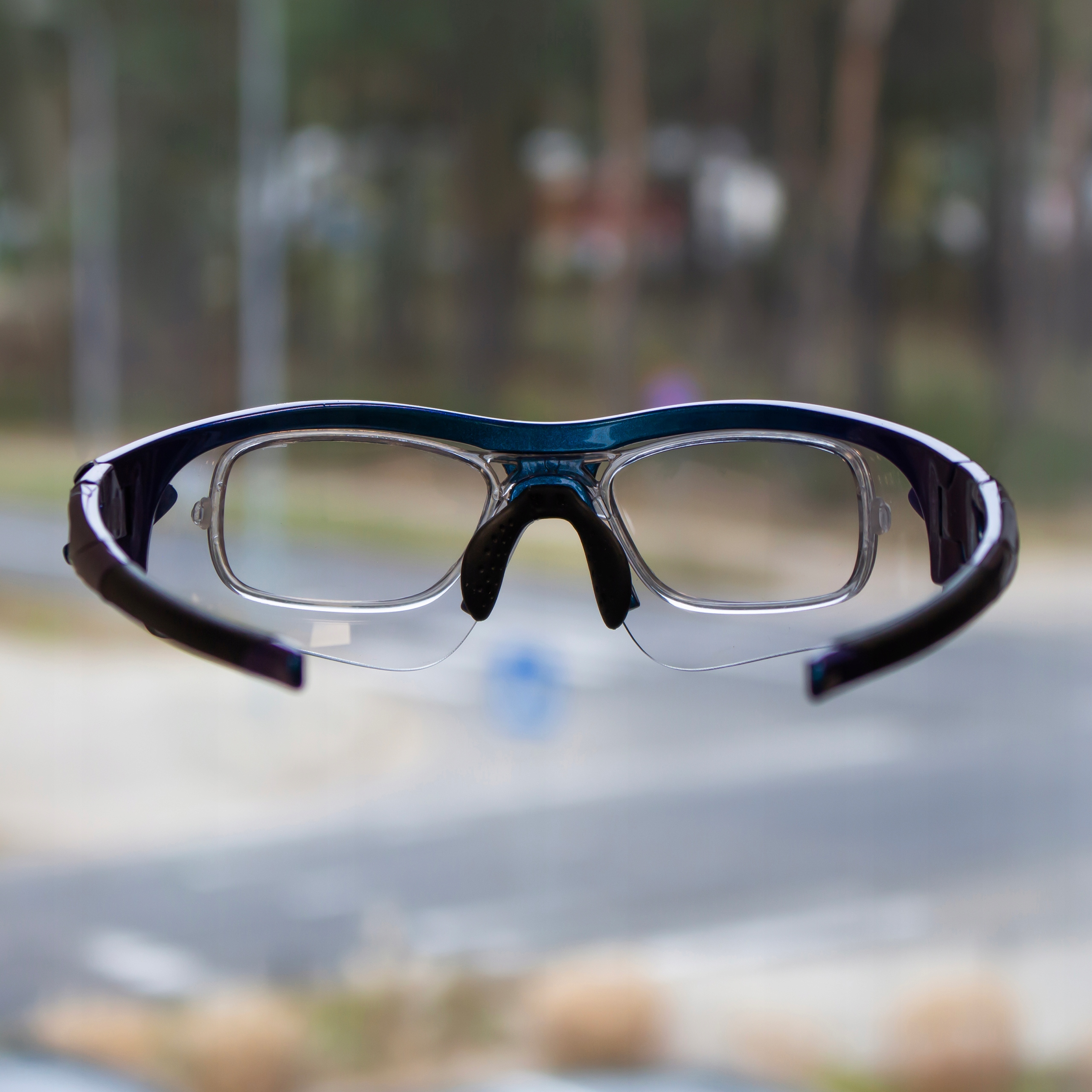 Eine Sportbrille mit klaren Gläsern und einem blau-violetten Rahmen. Verschwommener Hintergrund.
