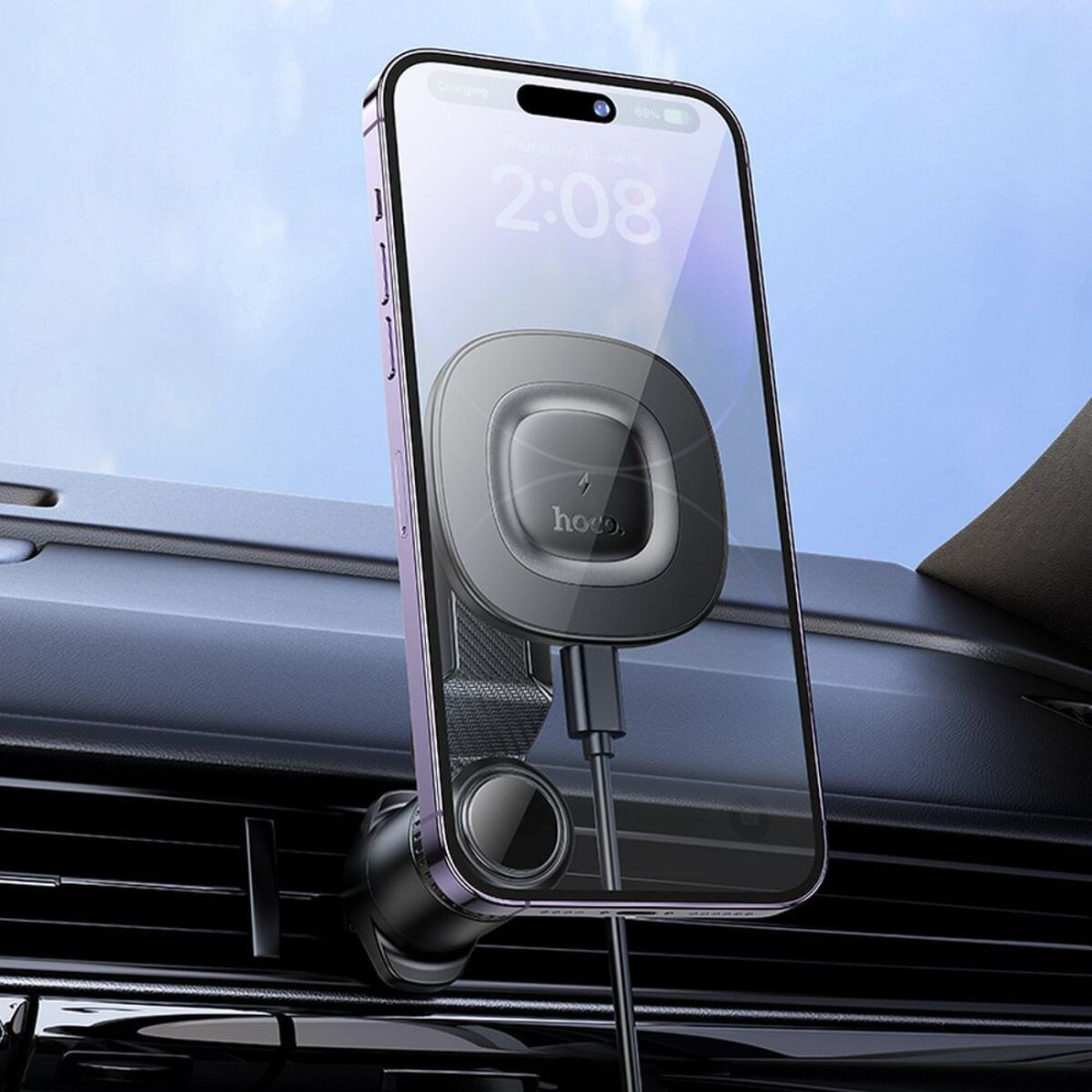 Telefoon gemonteerd in een auto, met oplaadkabel, tegen blauwe lucht.