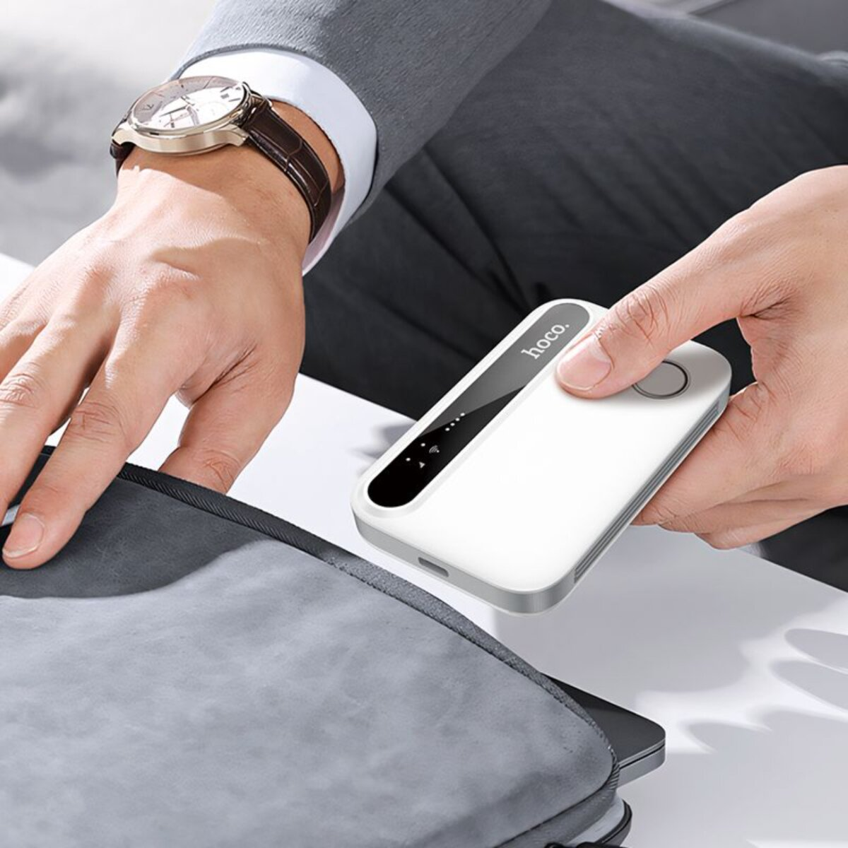 Persona che tiene in mano un router bianco. Orologio, laptop e borsa grigia. Sfondo sfocato.