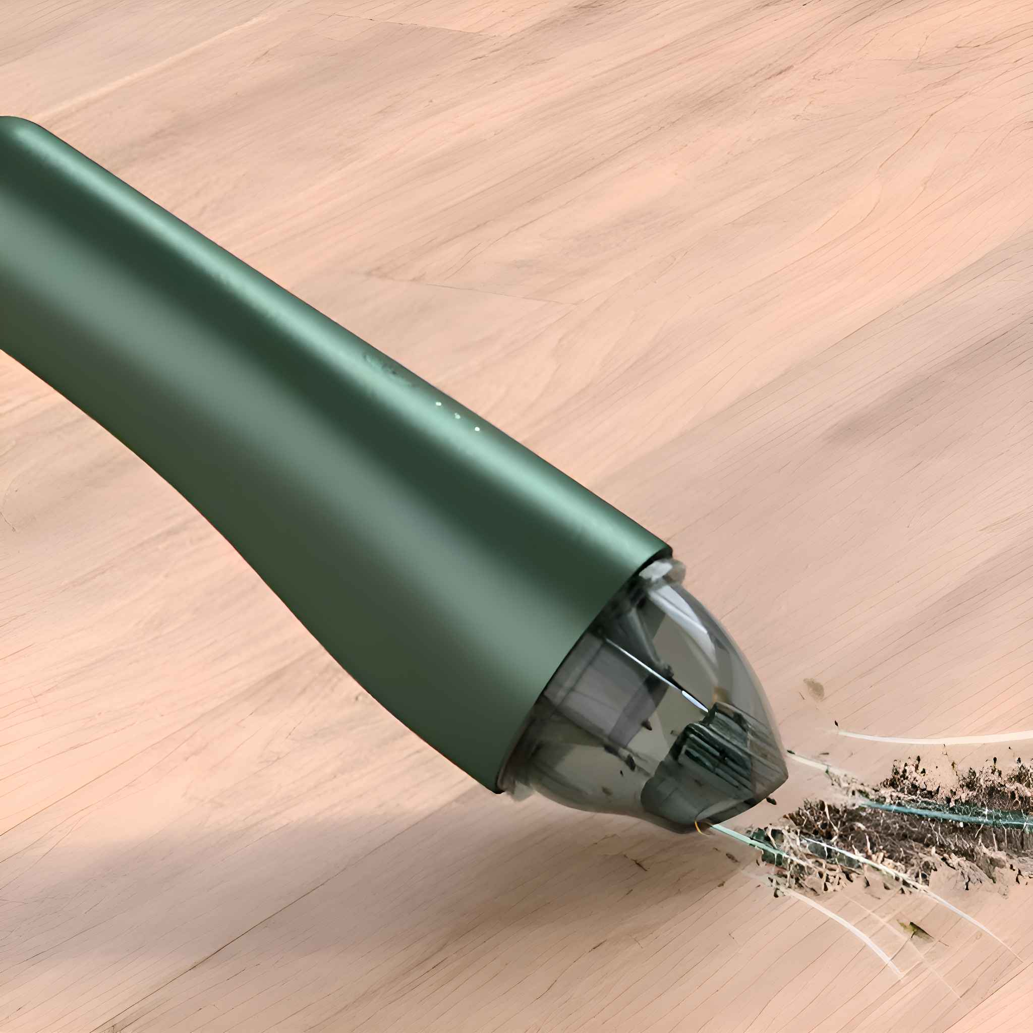 Grüner Handstaubsauger mit transparentem Aufsatz. Reinigt Schmutz auf Holzoberfläche.