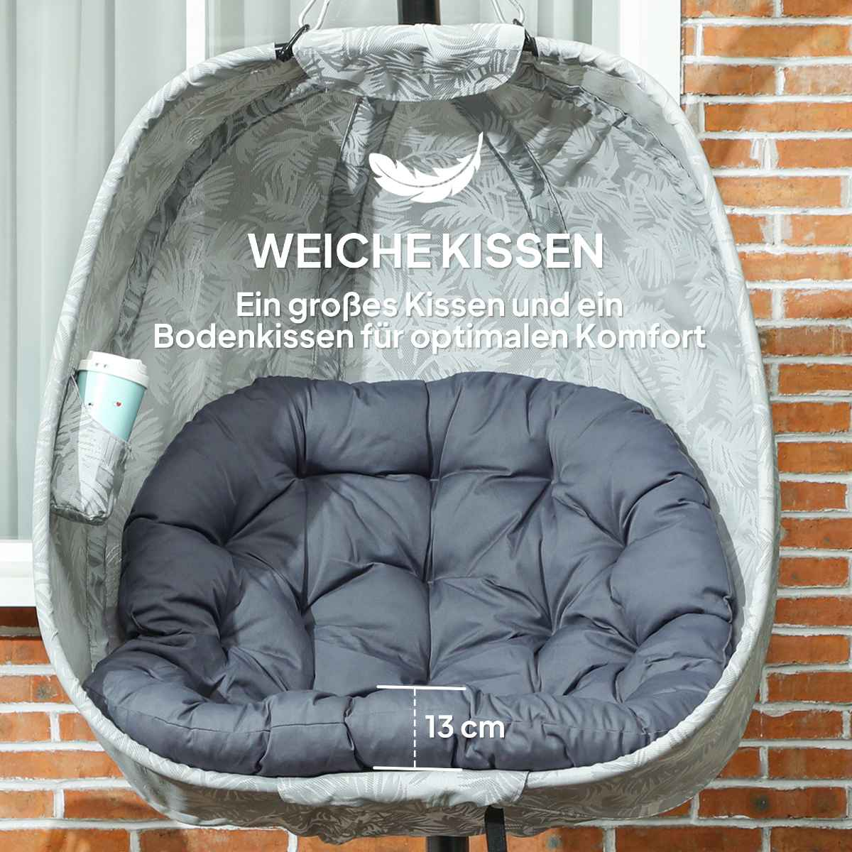 Hänge-Ei-Stuhl mit grauem Kissen. Auf Terrasse mit Backsteinmauer. Deutscher Text sichtbar.