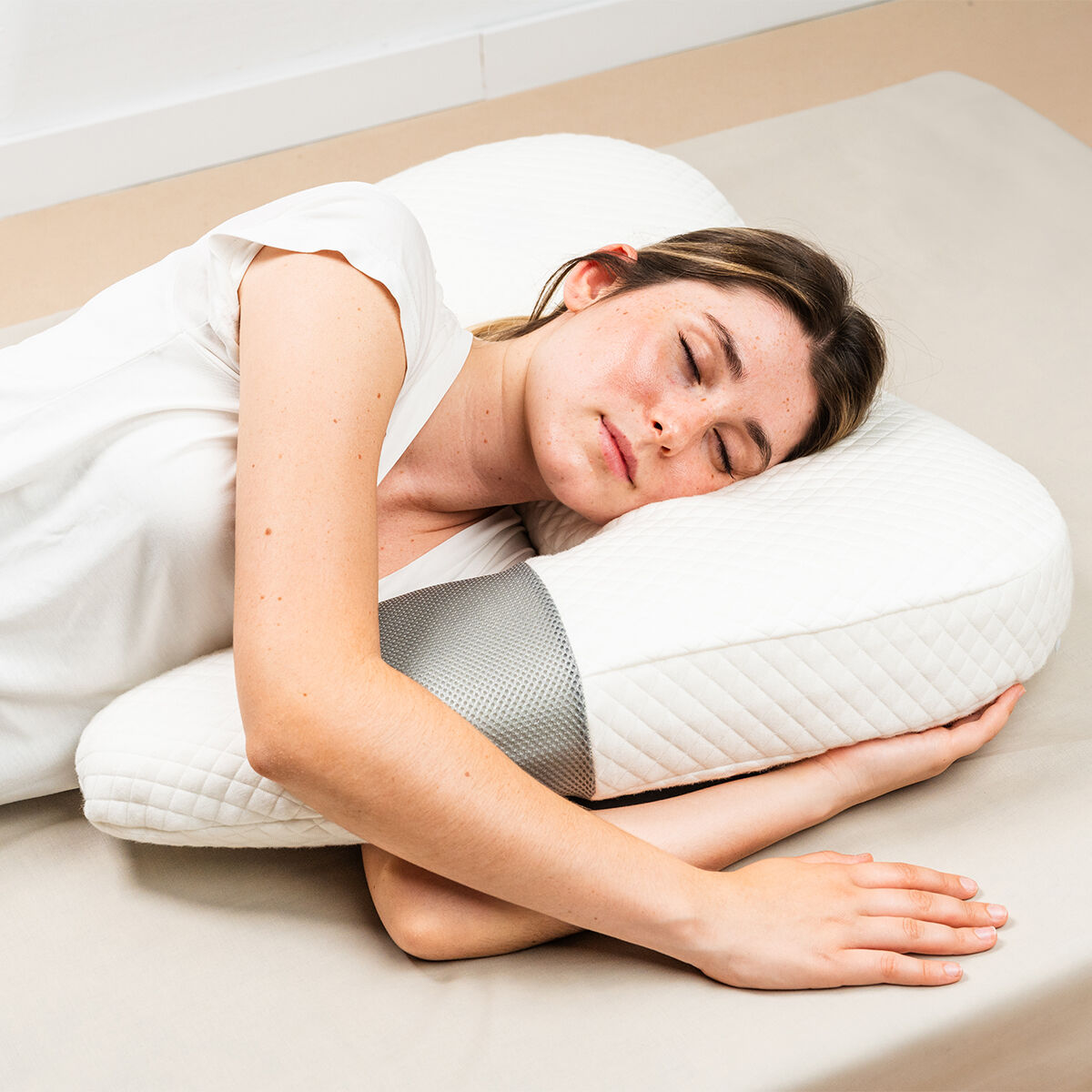 Frau liegt auf dem Bett, Kopf auf einem ergonomischen weißen Kissen mit grauen Seitenteilen.