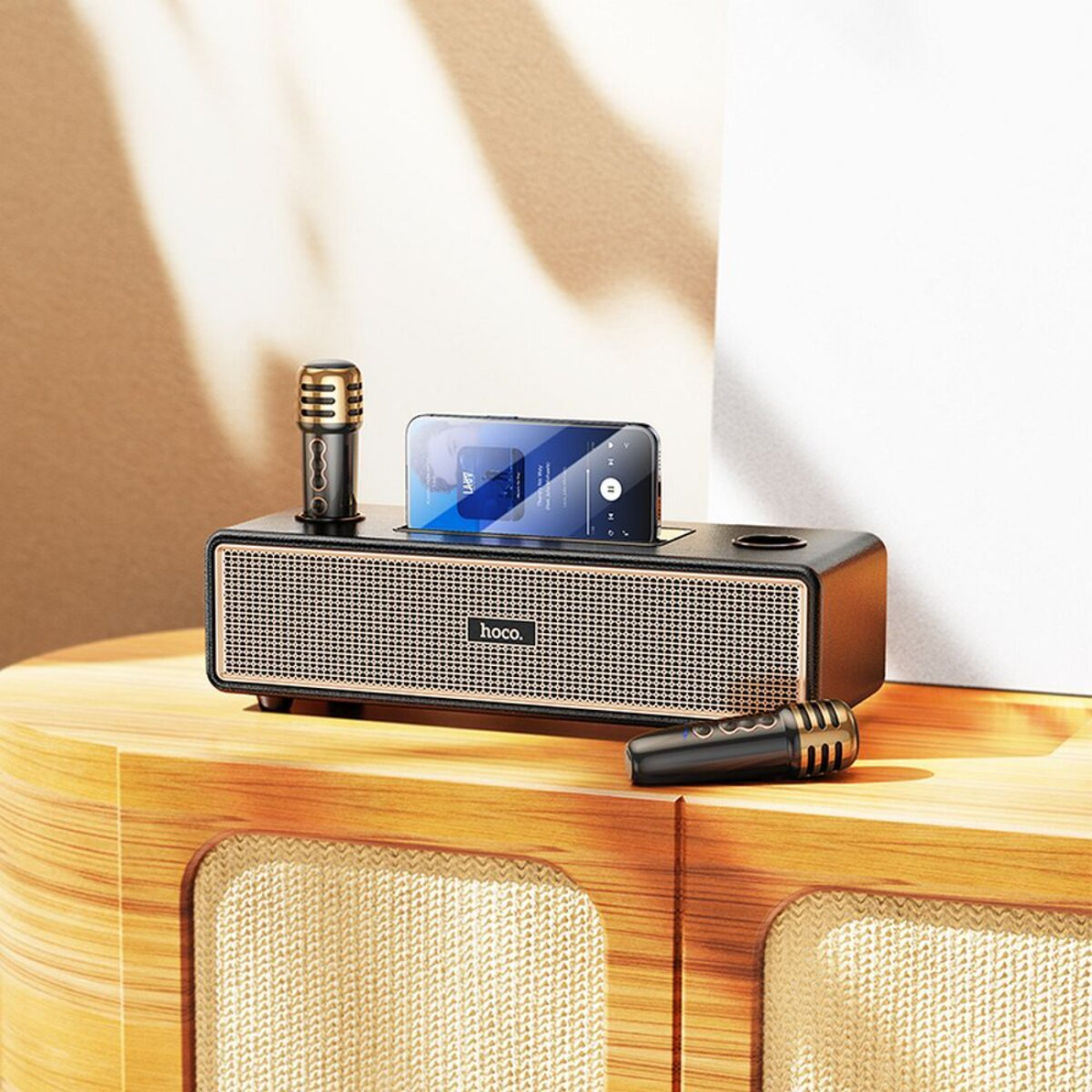 Un altoparlante nero con accenti dorati, che tiene un telefono. Due microfoni sono posizionati vicino su una superficie in legno.