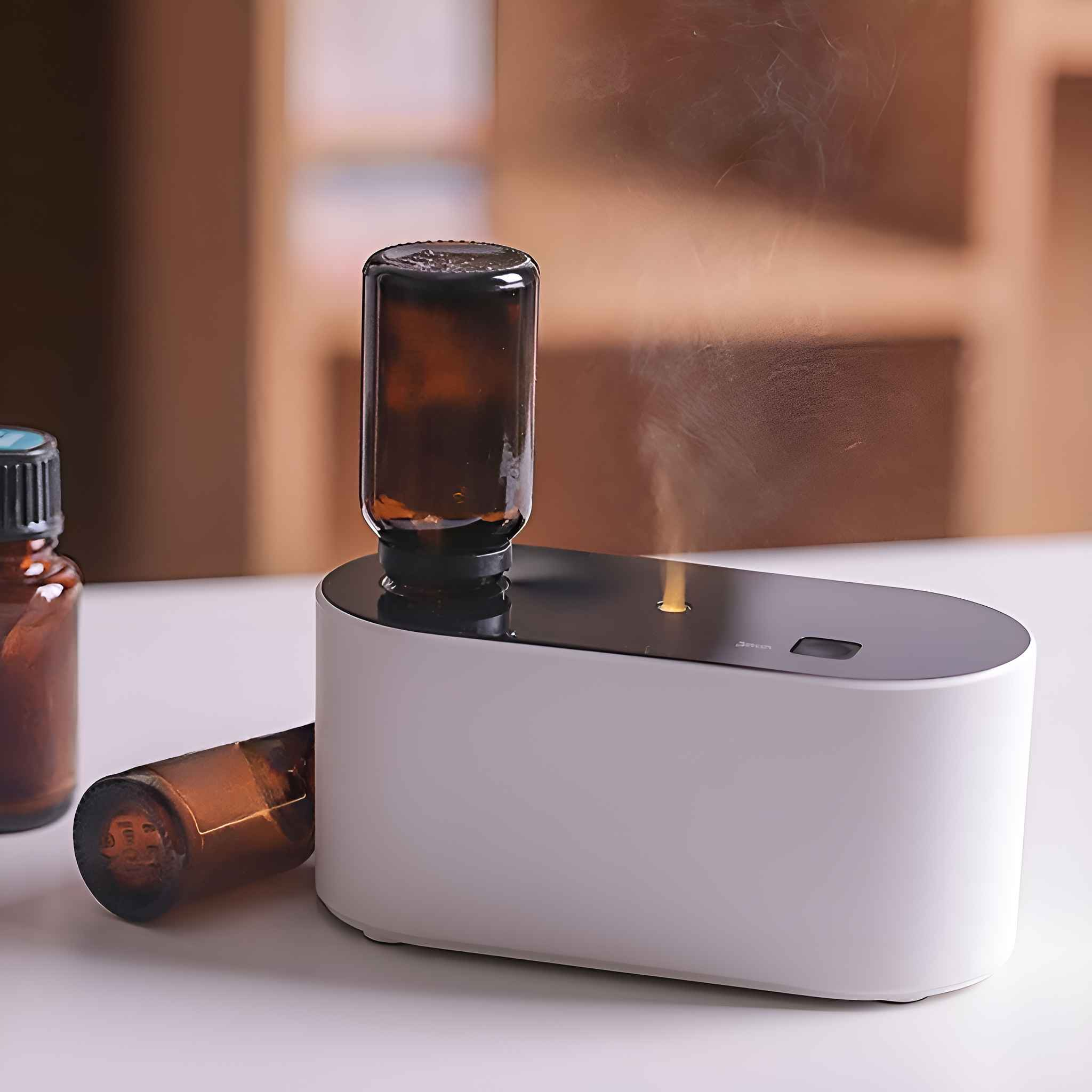 Ein Aromadiffusor mit weißer Basis und zwei braunen Glasflaschen, eine eingesetzt, die andere daneben.