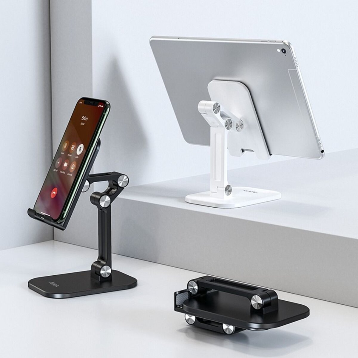 Drie telefoonstandaards: één met een telefoon, één met een tablet en één opgevouwen. Alle zijn zwart en wit.