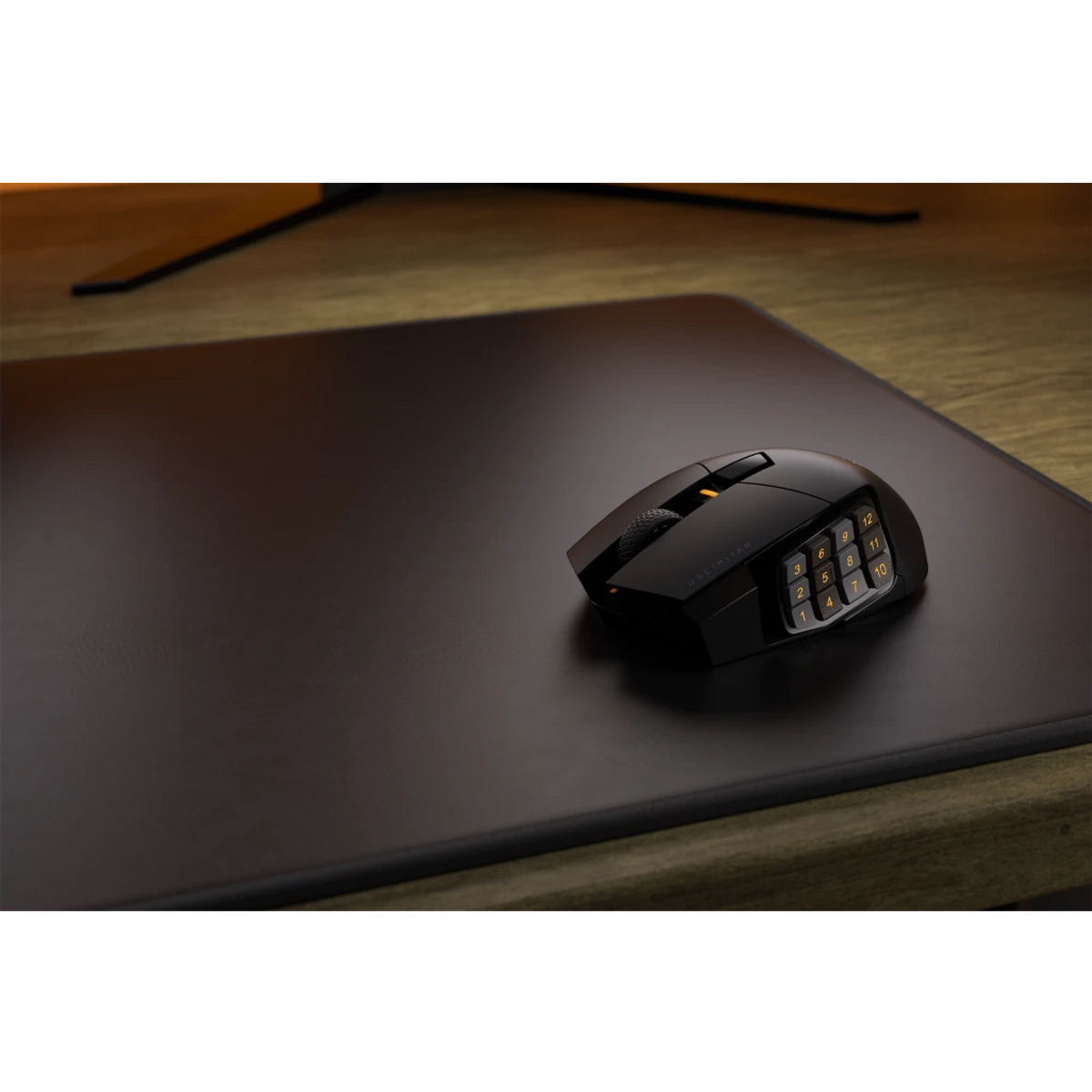 Black mouse on a black mat. Wooden table in the background and a monitor. Dark setting.