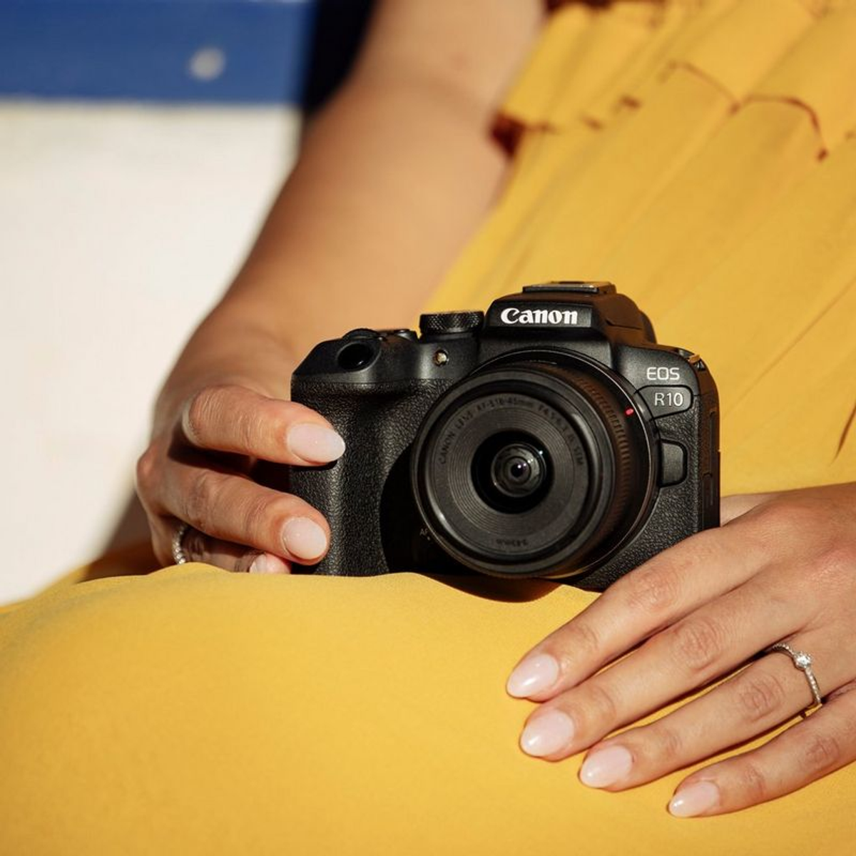 Eine Person hält eine Canon-Kamera mit Objektiv vor einem gelben Kleid.