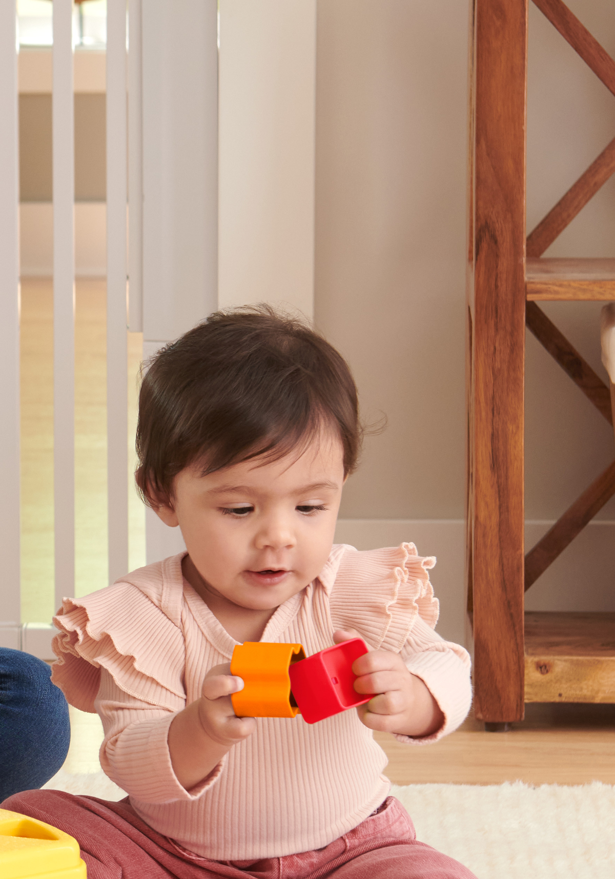 Ein Baby sitzt und hält zwei bunte Blöcke, einen roten und einen orangenen Würfel.