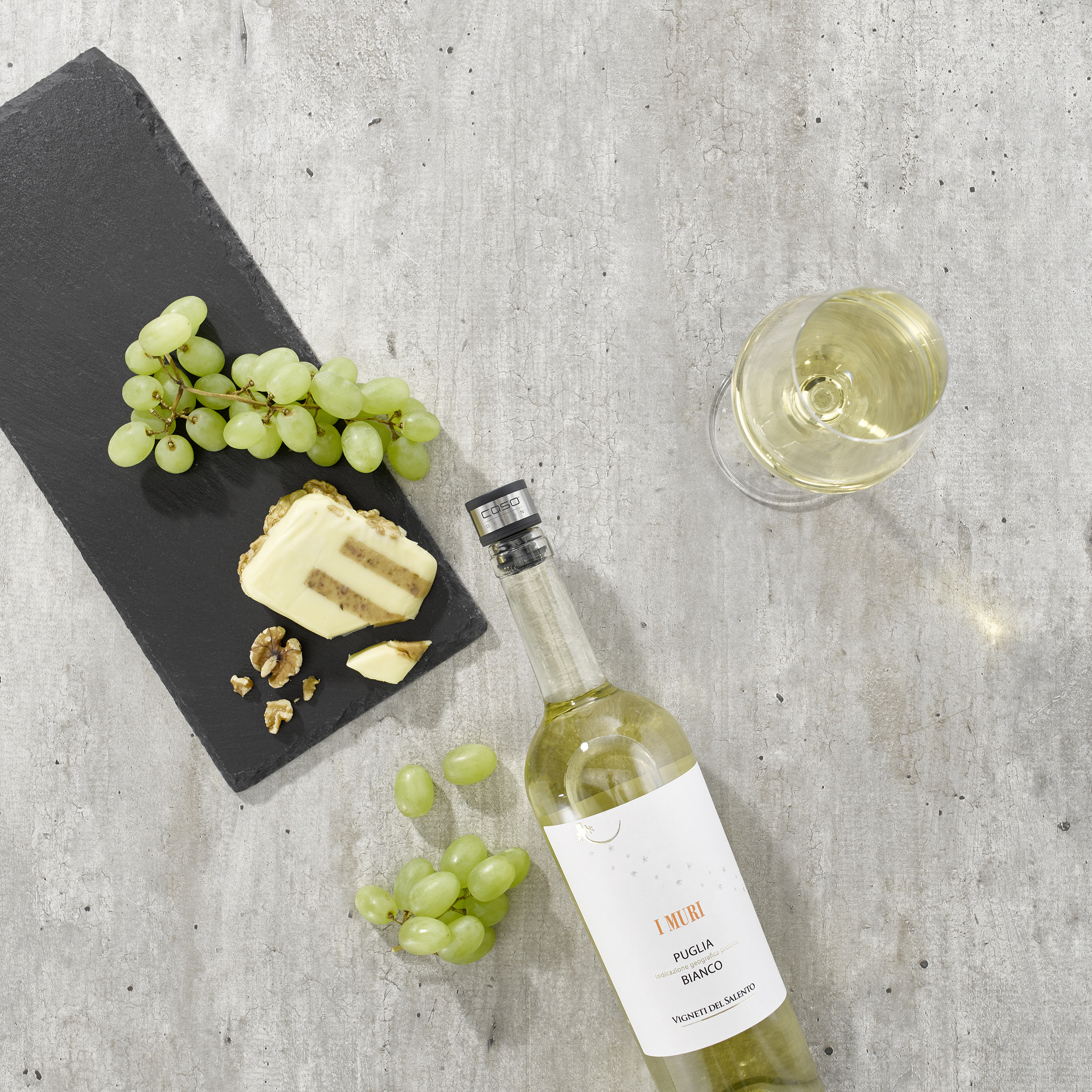 Draufsicht auf Wein, Käse, Trauben und Nüsse auf einer grauen Oberfläche.