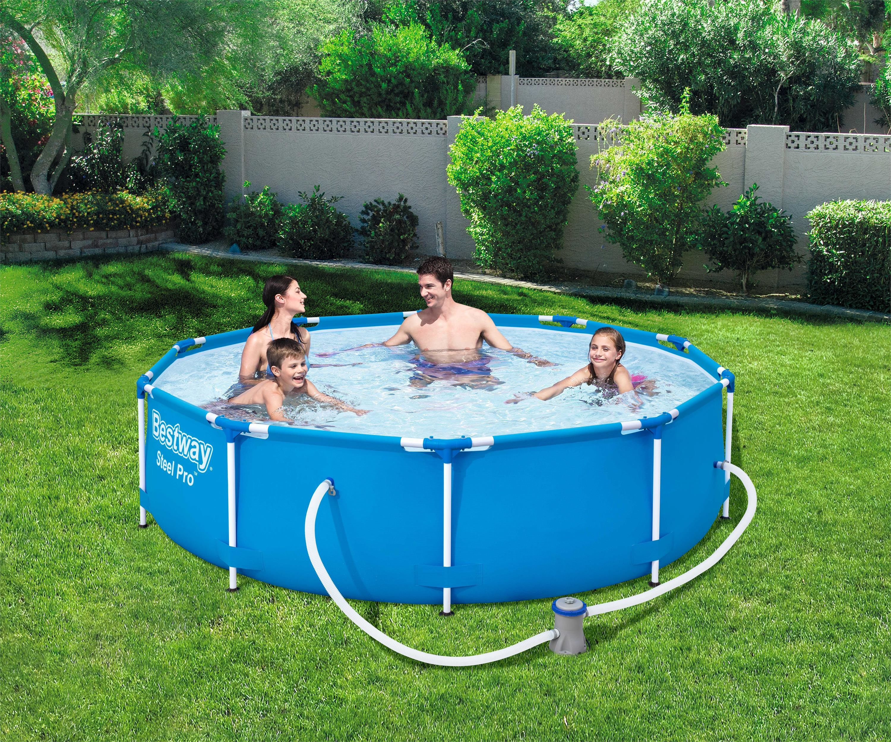 Famille dans une piscine bleue. Pelouse verte, arbres et mur crème en arrière-plan.