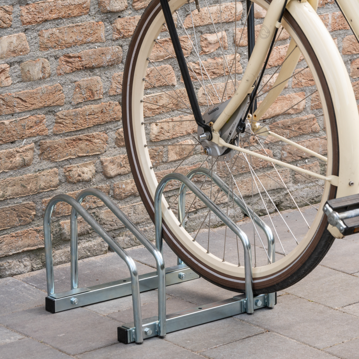 Fietswiel vastgezet in een fietsenrek met een bakstenen muur op de achtergrond.