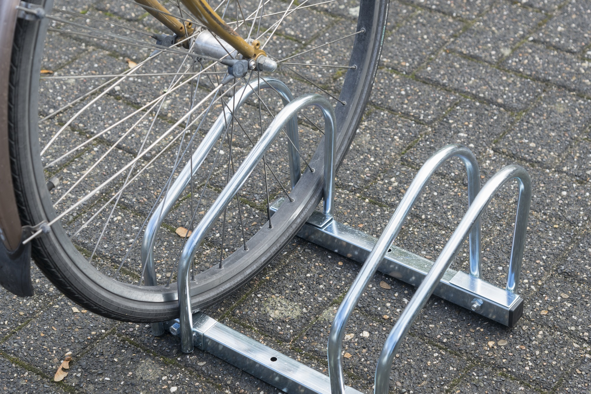 Een fietswiel in een metalen fietsenrek op een bakstenen oppervlak.